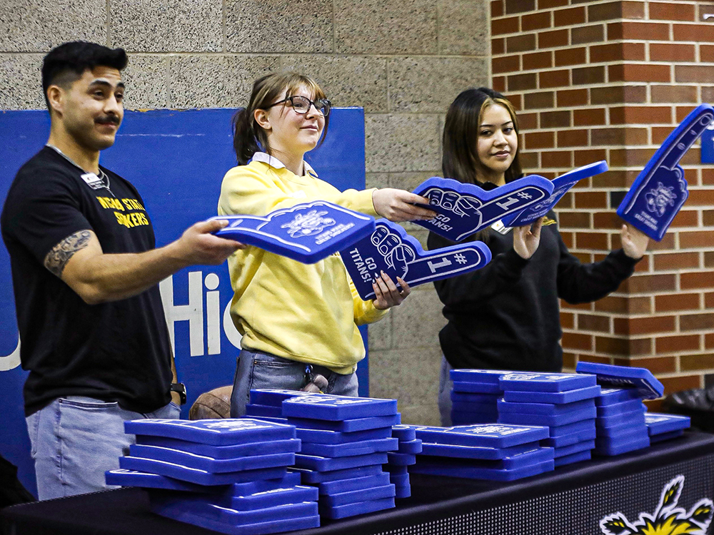 Ambassadors Rafael Guereque, Lin Lindstrom and Kassandra Rodela-Marrero pass out foam fingers at a Wichita South High School basketball game.