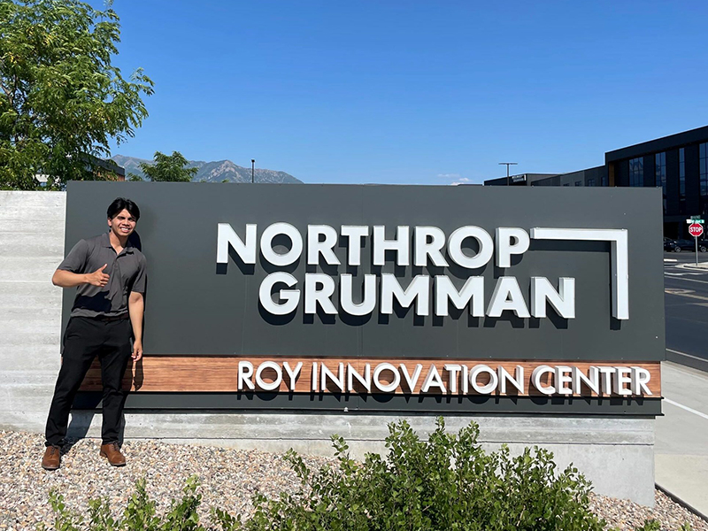 Eliseo poses with a Northrup Grumman Sign at his internship in California