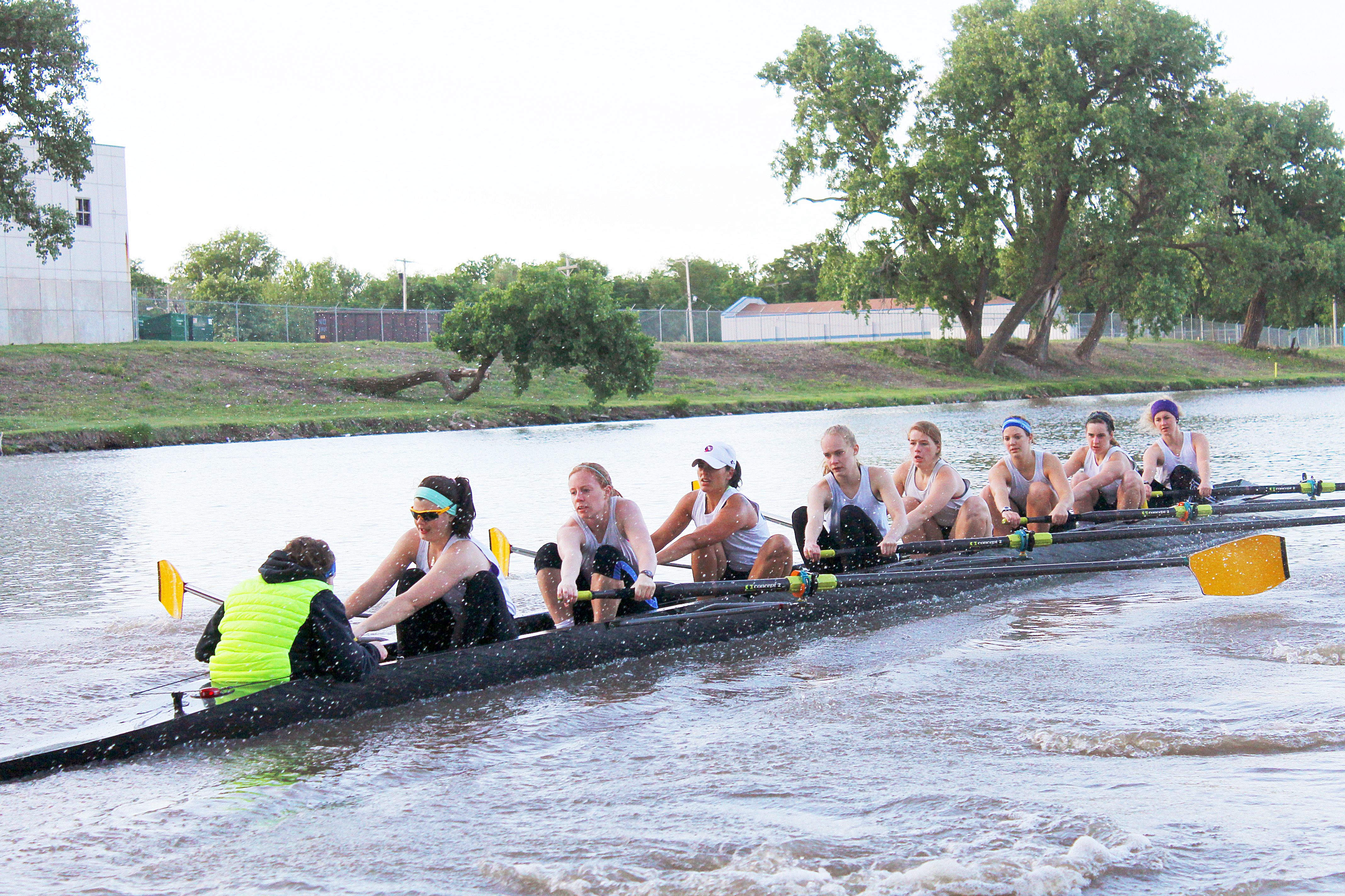 Women's eight rowing down the river. They are working hard. The rowers face us, the coxswain faces away.