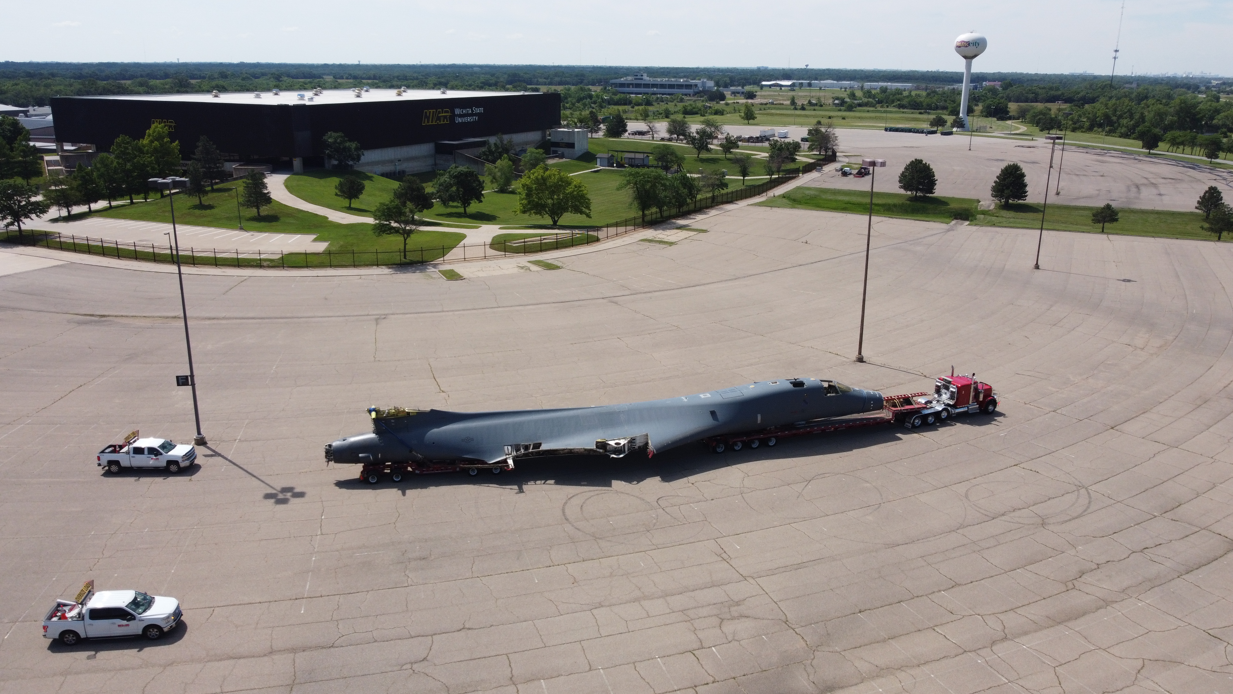 Aeral view of a B-1 aircraft (minus the wings) being towed by a semitruck turning a corner.