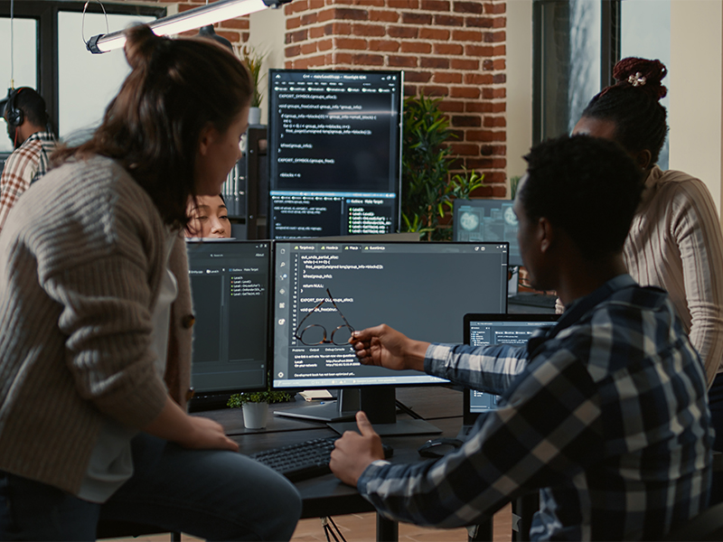 Photo of three people reviewing code on a monitor