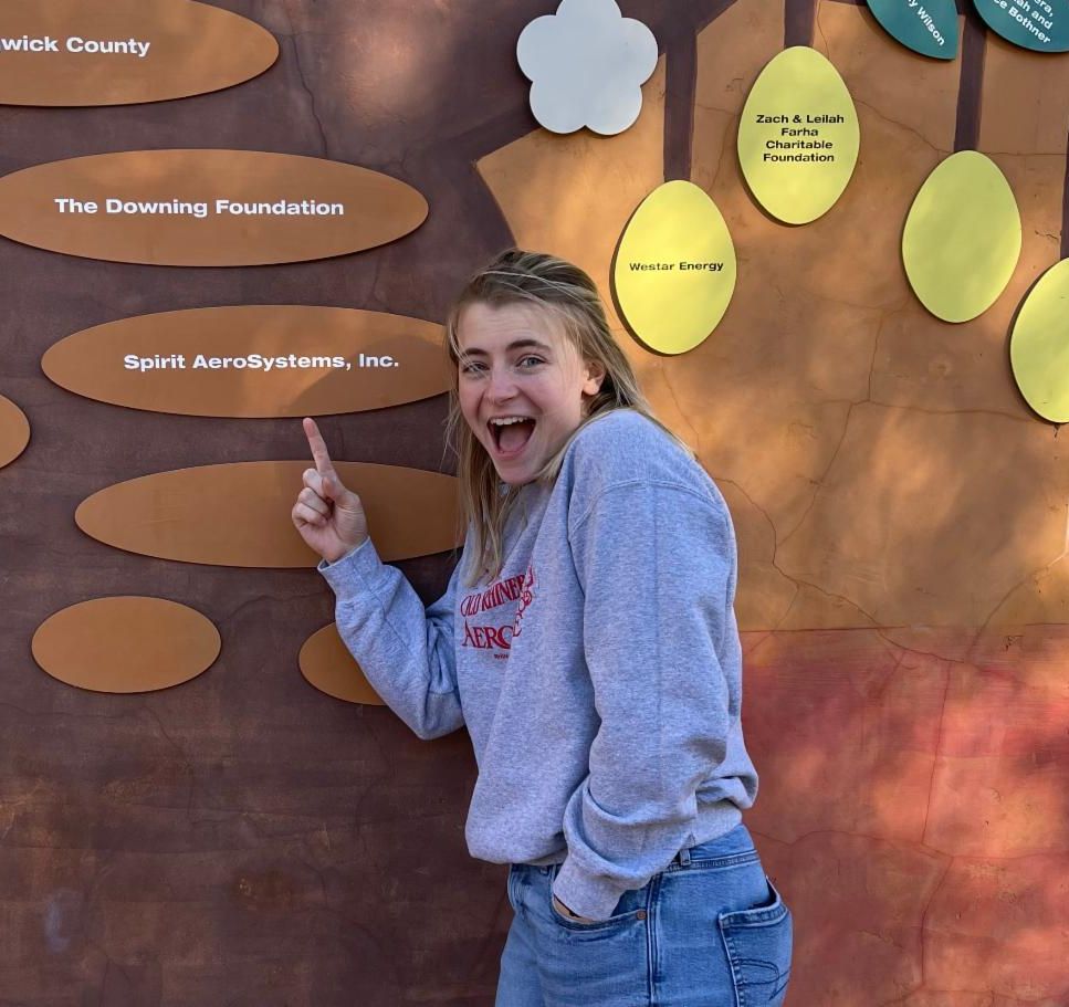Photo of Caroline Ruden pointing at a Spirit Aerosystems sign