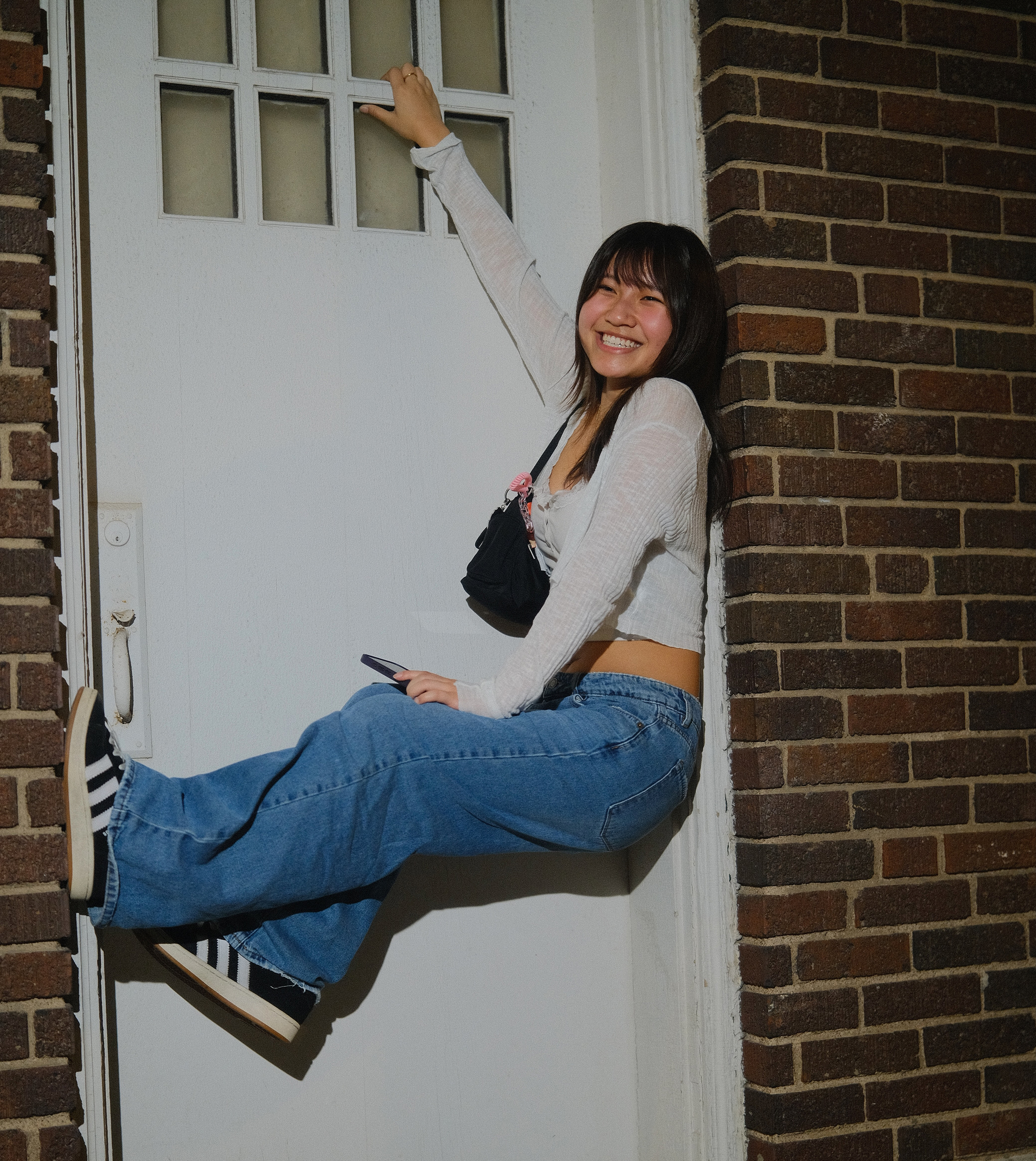 Photo of Christine Nguyen hanging from an old white door frame in a brick wall.