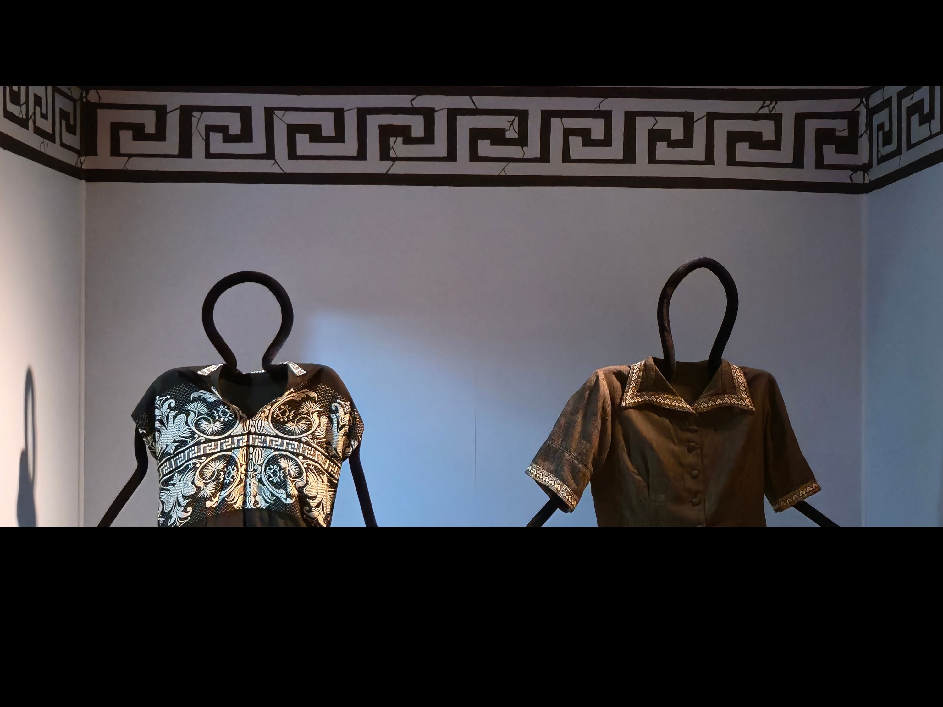 Open case with blue background with a meandering patter across the top. Mannequins with garments on them are on display.