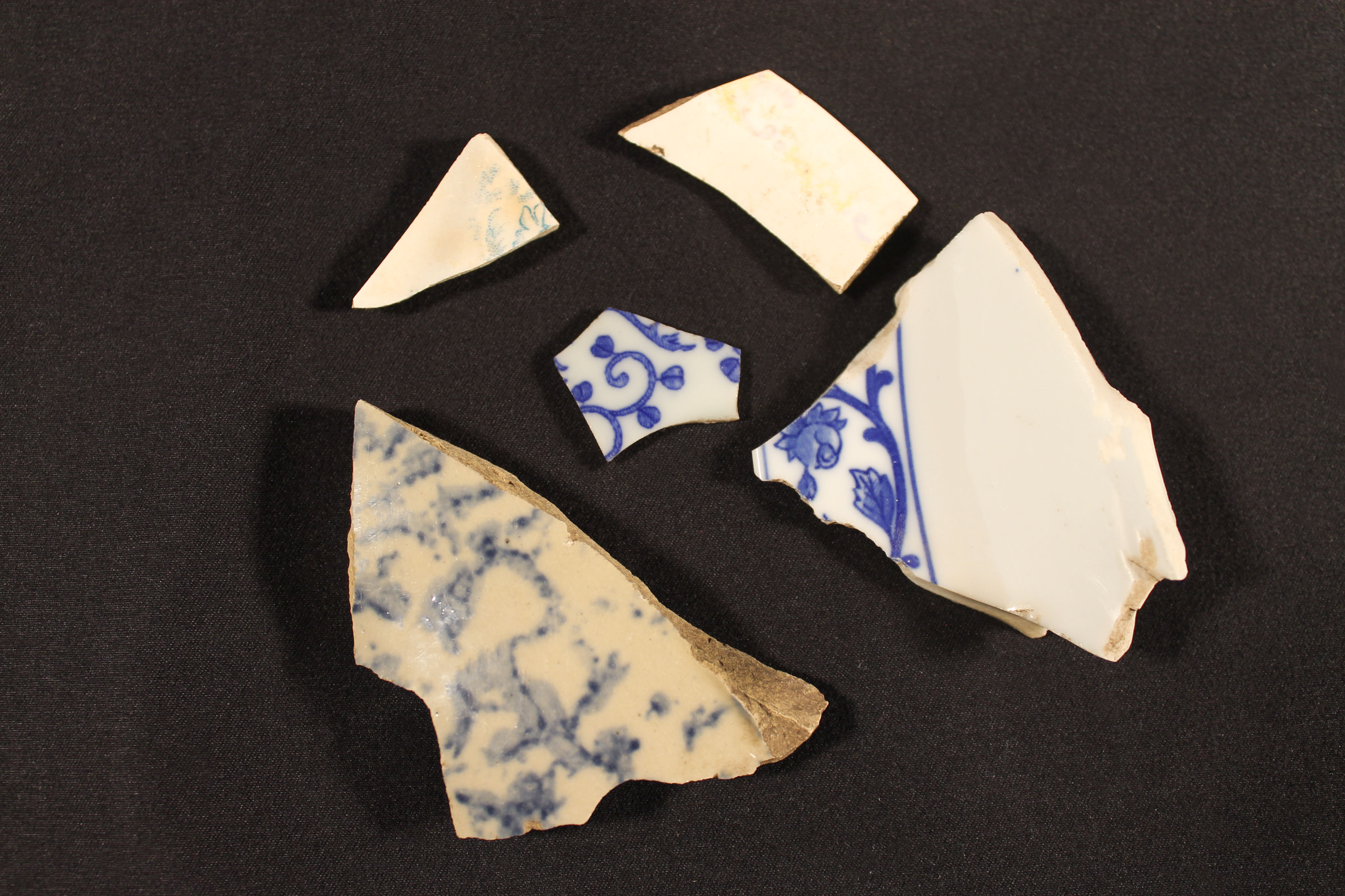 Five broken pieces of white pottery that have blue flowers on them