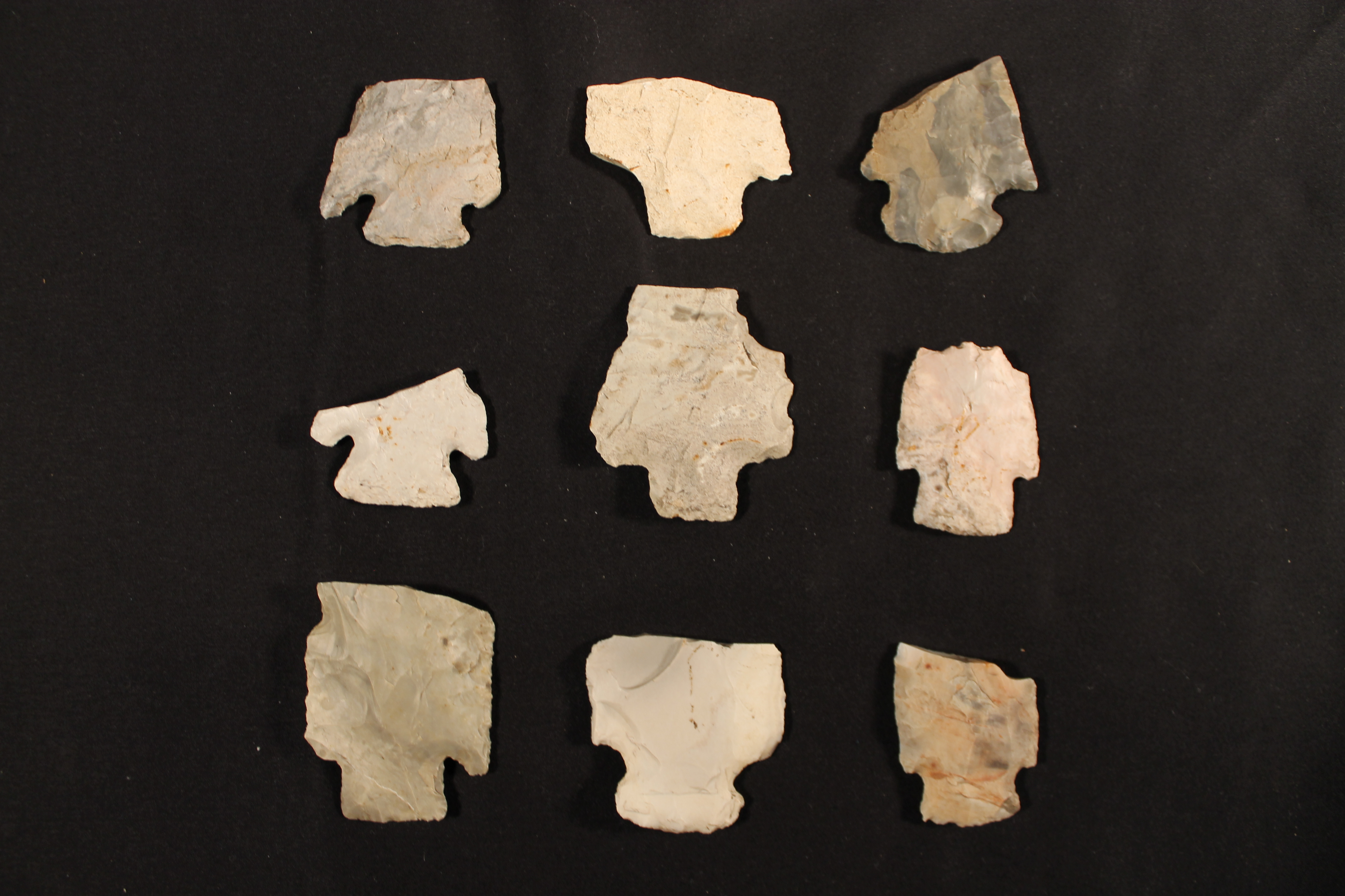Nine arrowheads with notched sides at the bottom. All of their top points have been broken off.