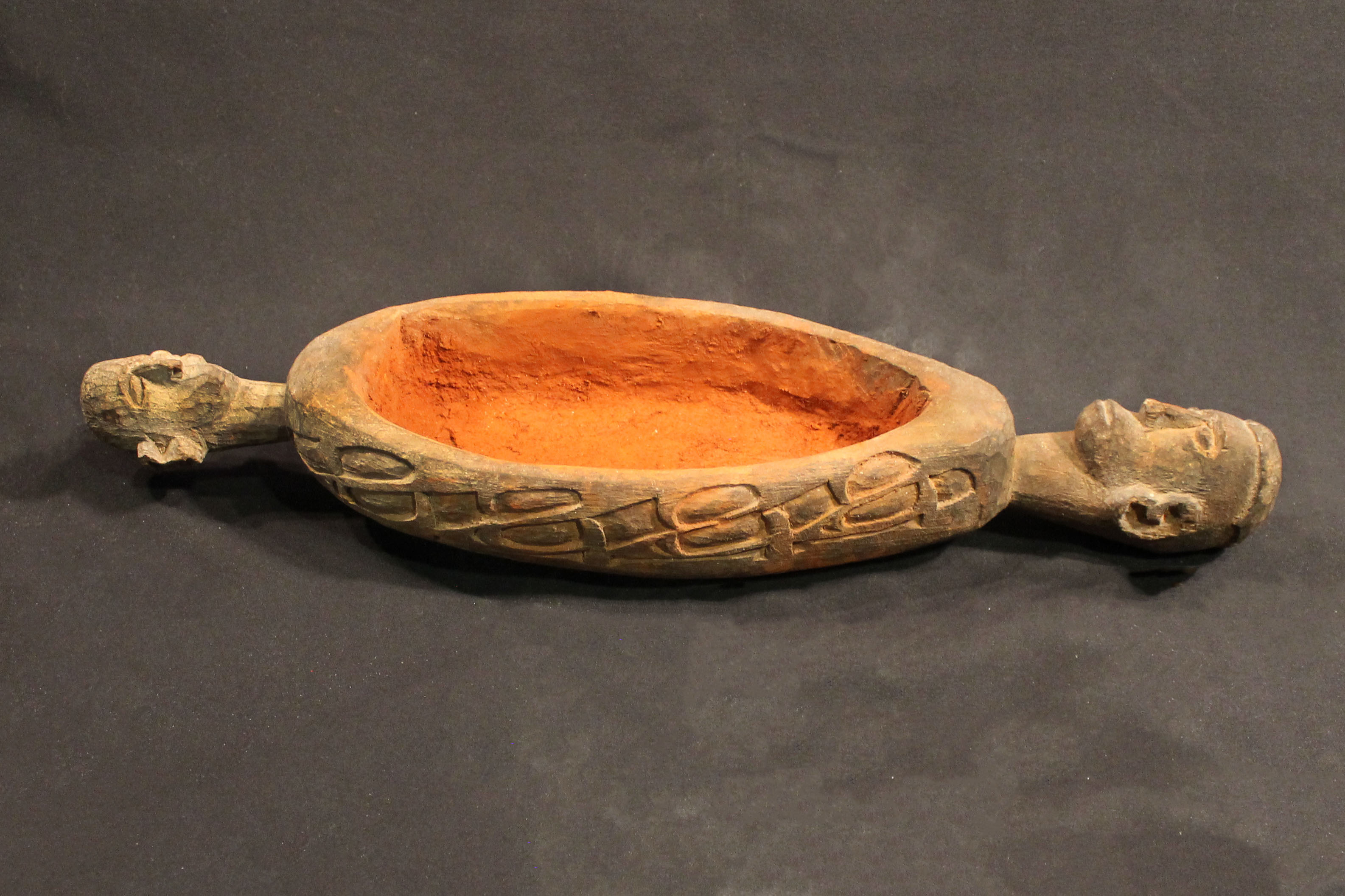 Small bowl with a human head carved on either end. The side is covered with red pigment.