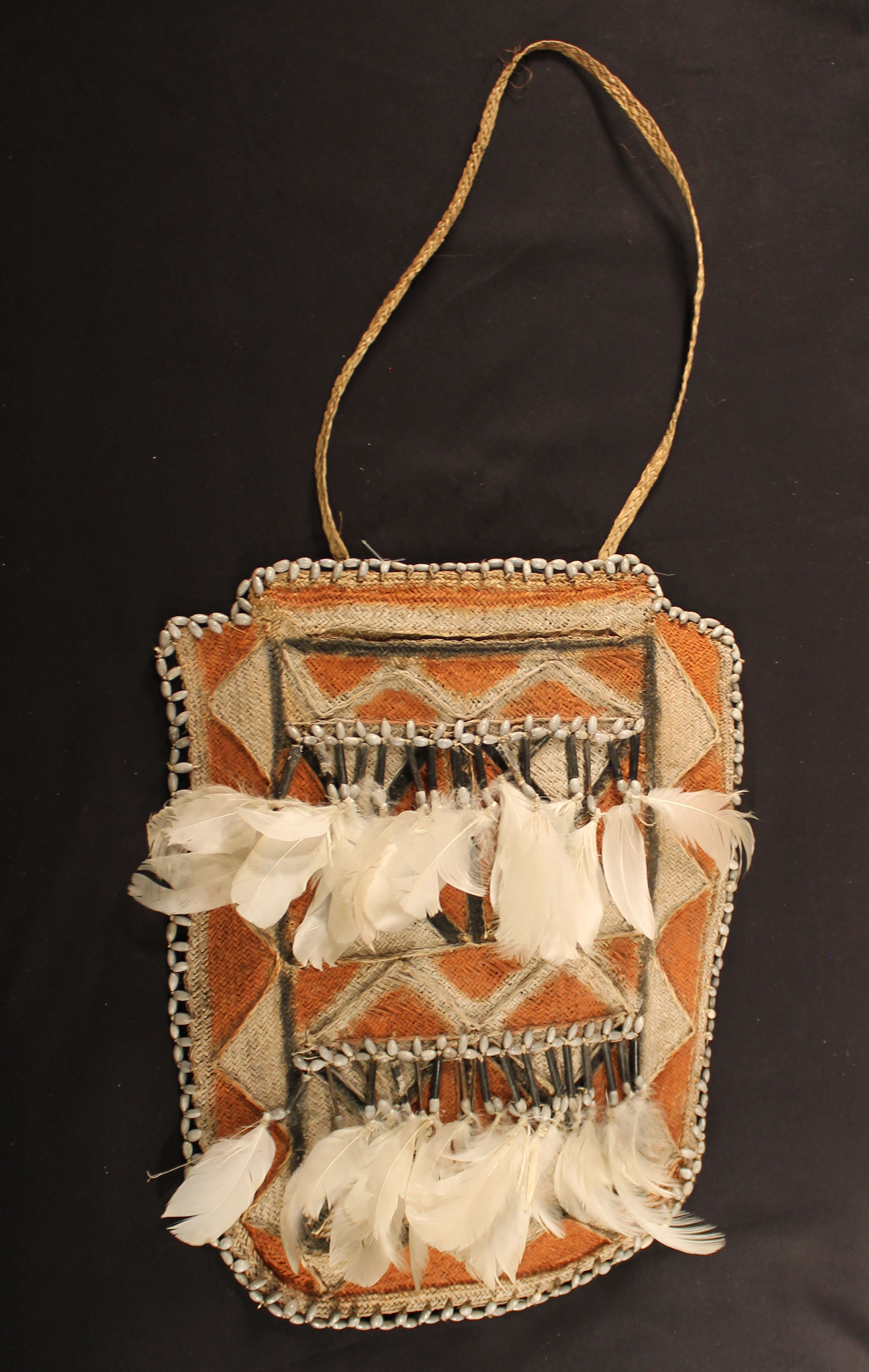 Woven bag with symbolic designs covered with an orange and white triangle and has white feather trim