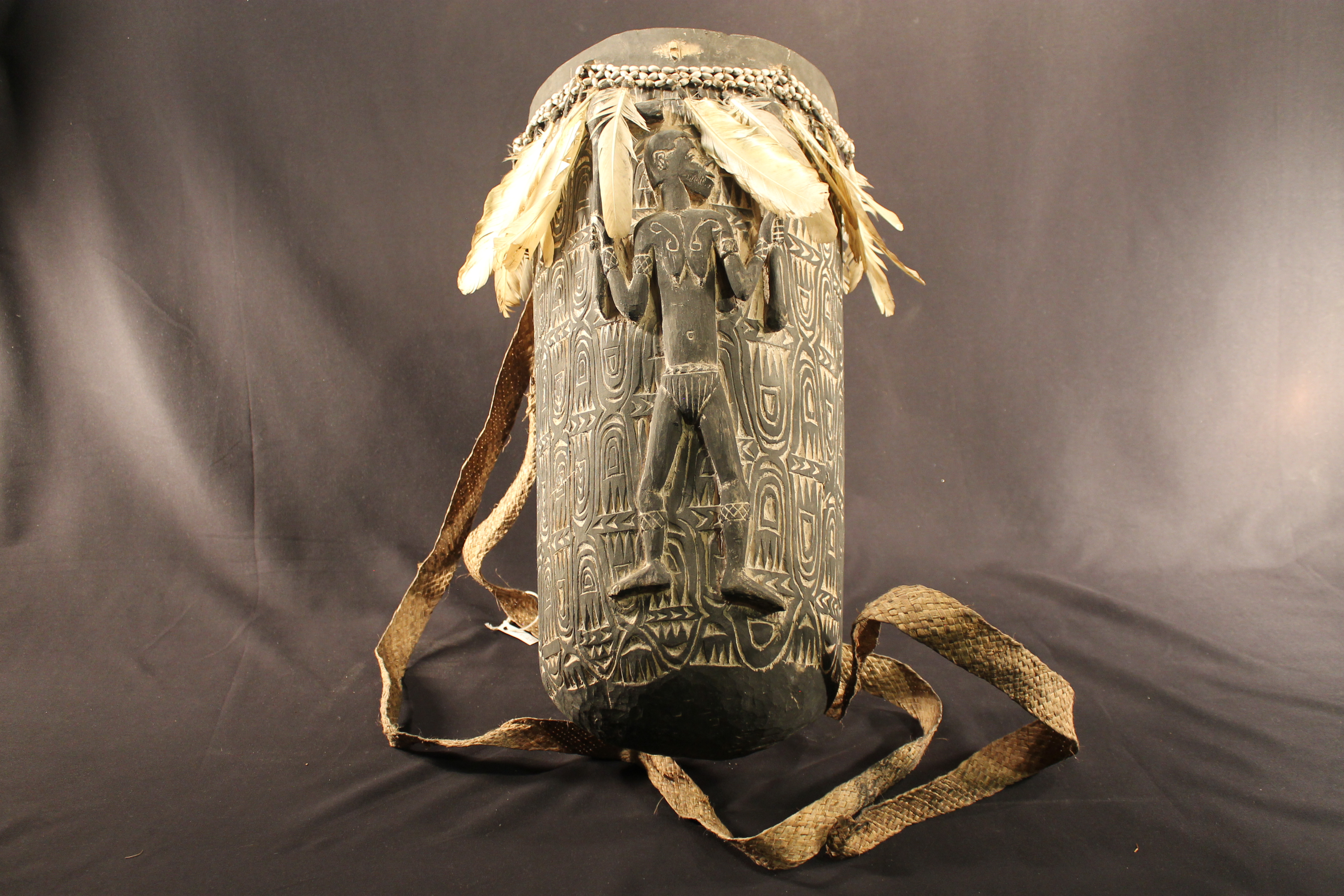 Carved wooden basket with woven attached traps. The front depicts a man. A band of seed beads and feathers are attached. 