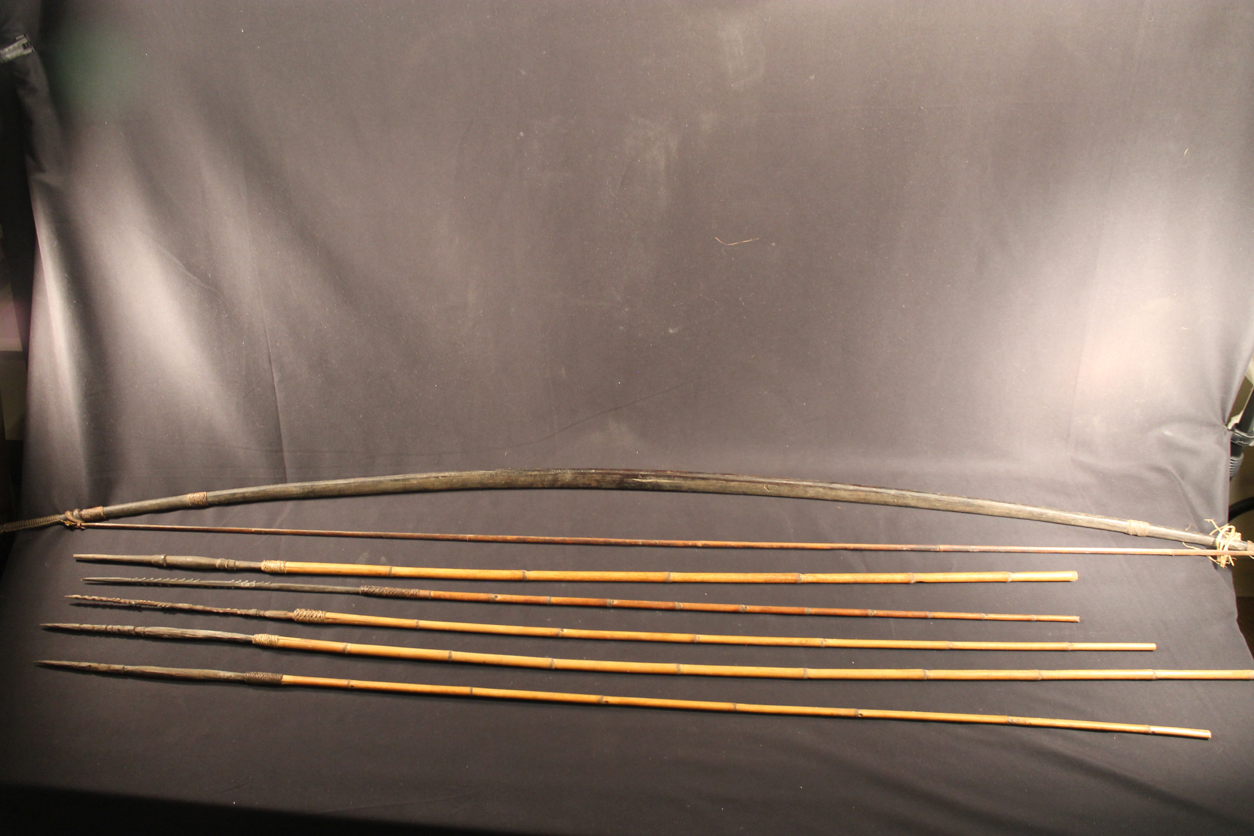 Dark brown wood bow that has a claw attached to the string. Also, there are five bamboo arrows.