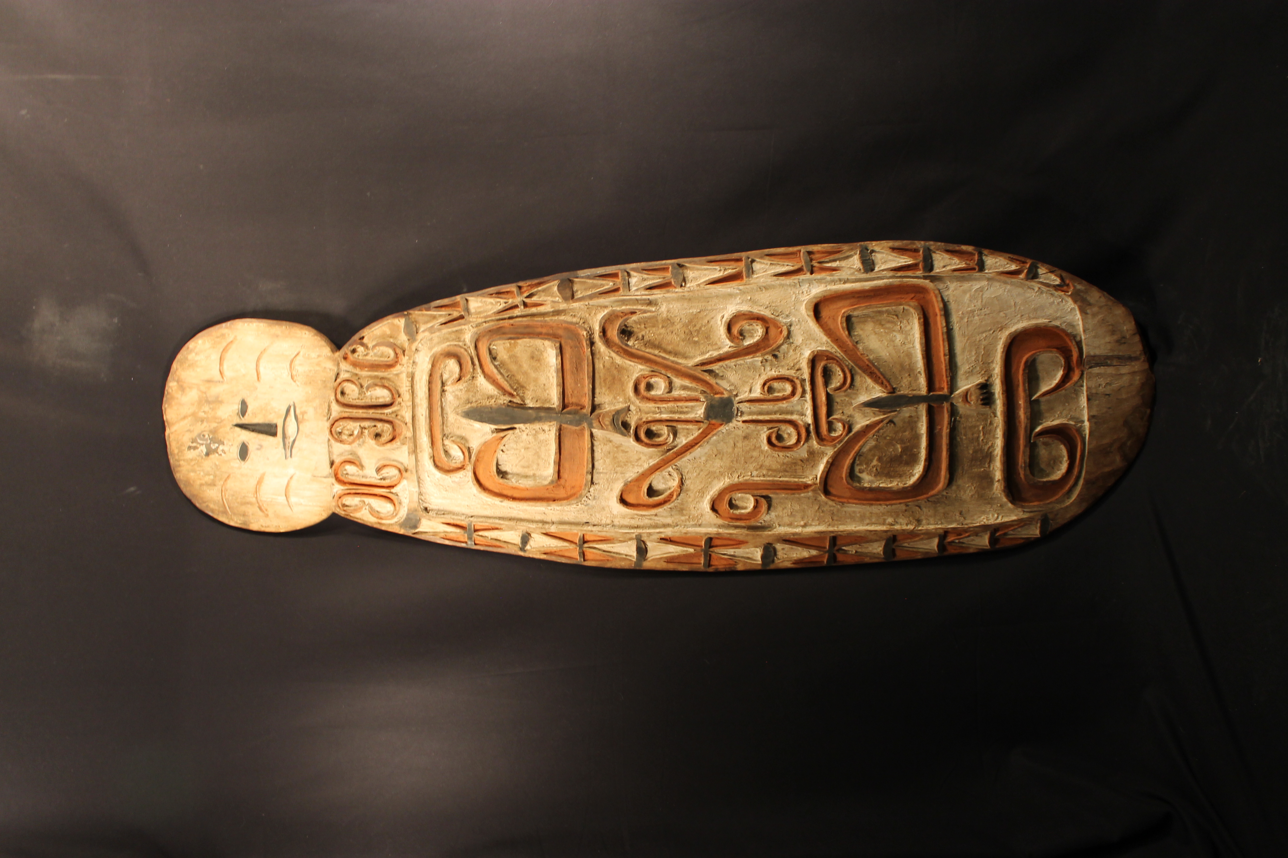 Large carved shield with “B” and “P” shaped designs. The shield has a face carved into the top.
