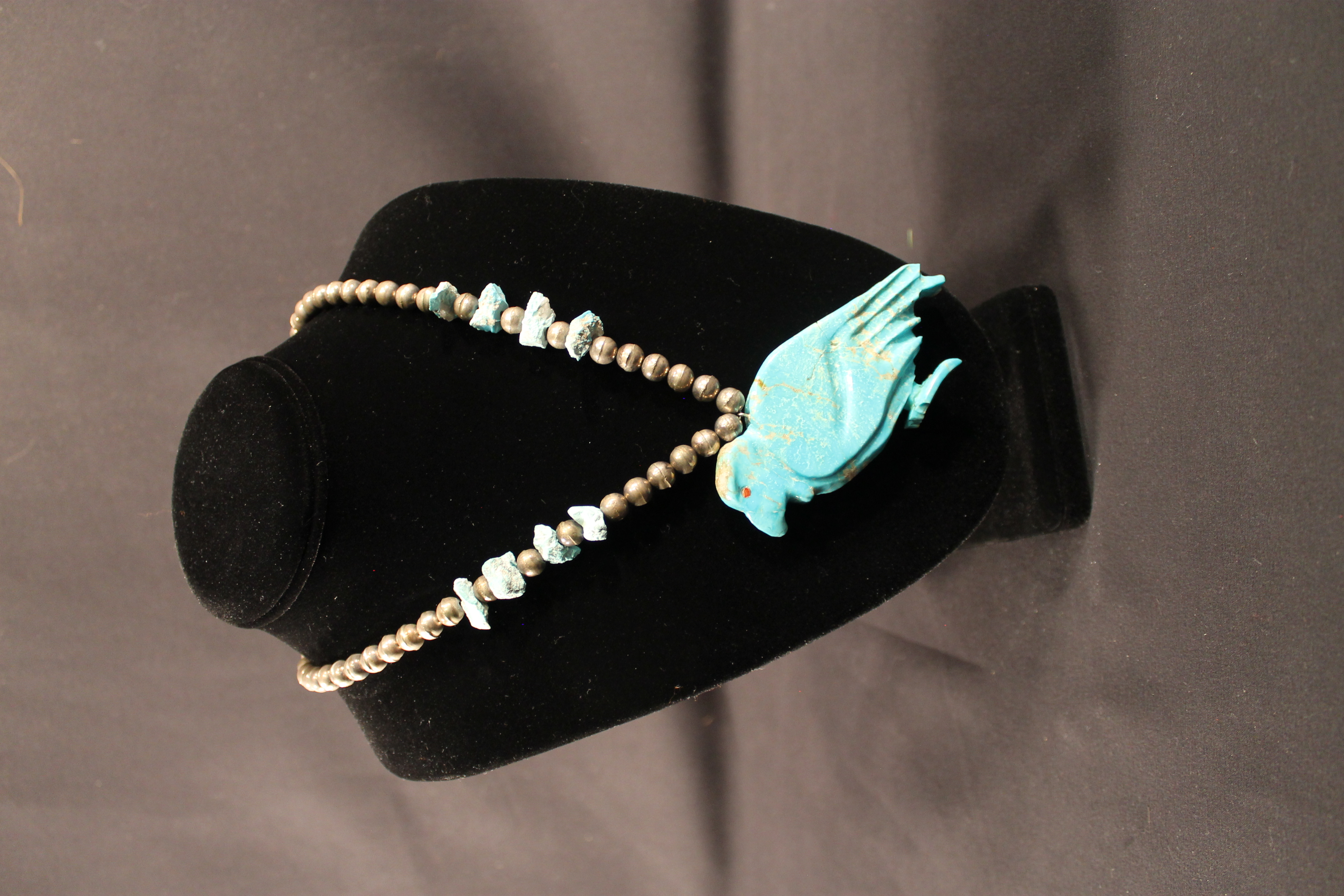 urquoise bird necklace that is comprised of brass-colored beads. At the bottom is a turquoise eagle pendant, which has a visible seam from being repaired