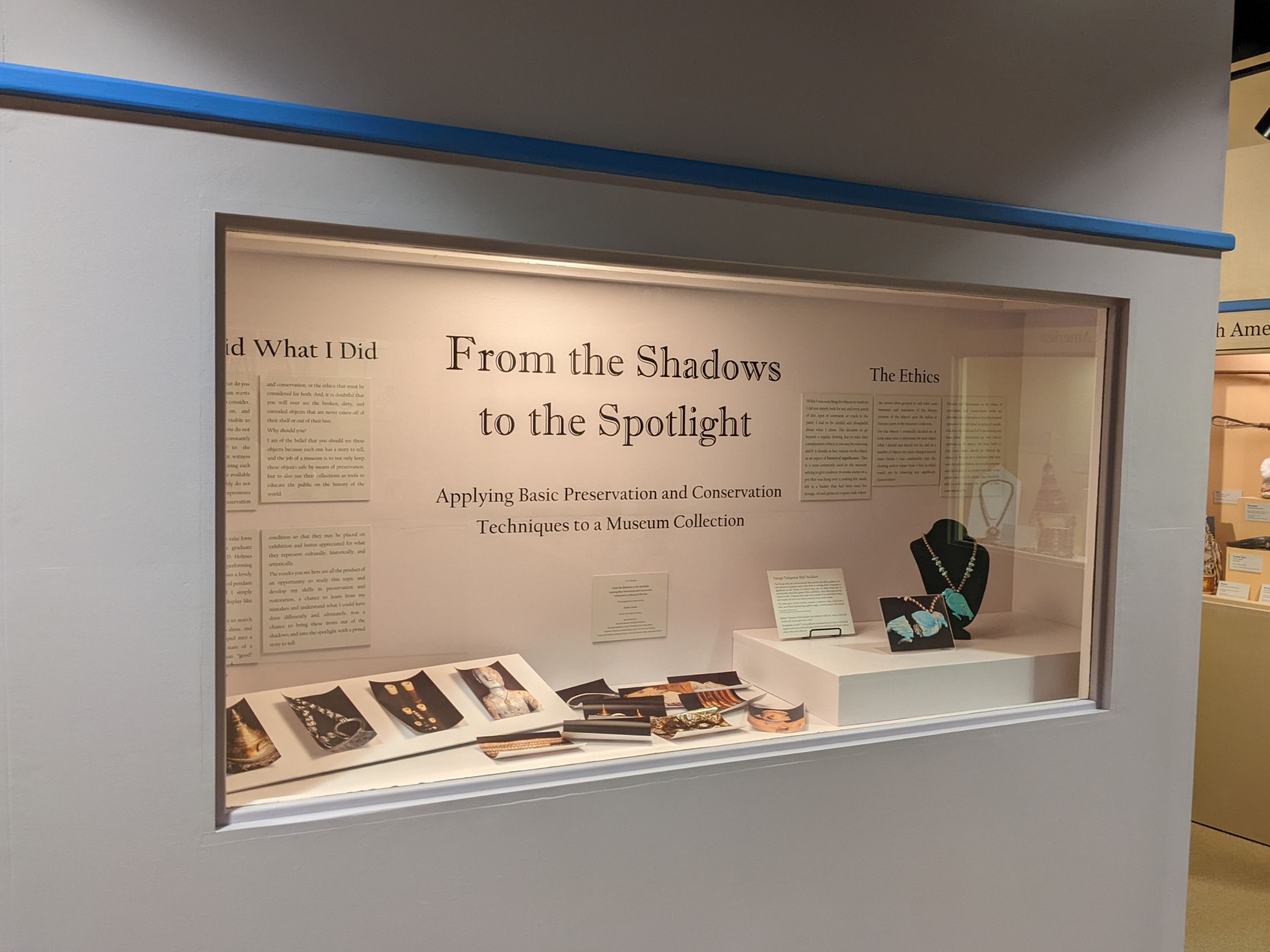The exhibit narrative starts on this case. This features the curation statement on the project and the ethics behind it. Below this text is a display of various close-up photographs of objects featured in exhibit cases. On the far right, the first object is a turquoise bird necklace.