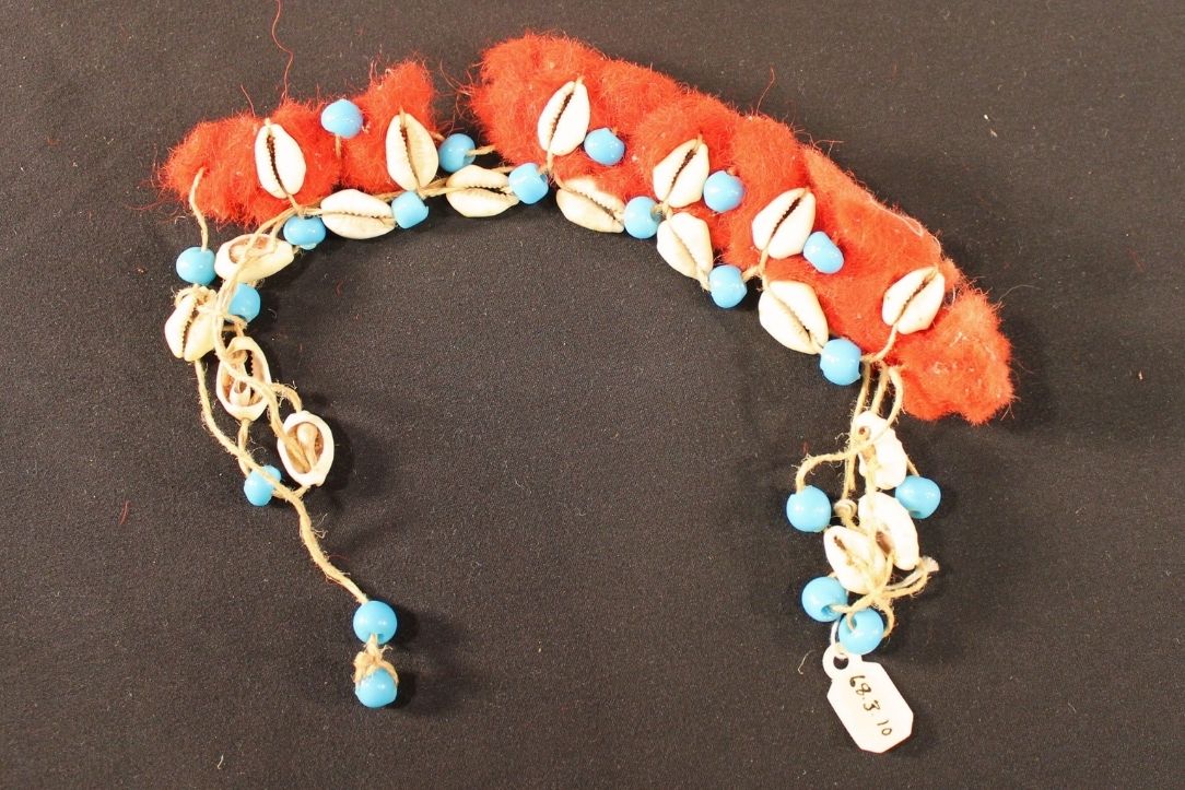 Bracelet is cowry shells and blue beads attached with twine to the dyed red wool band.