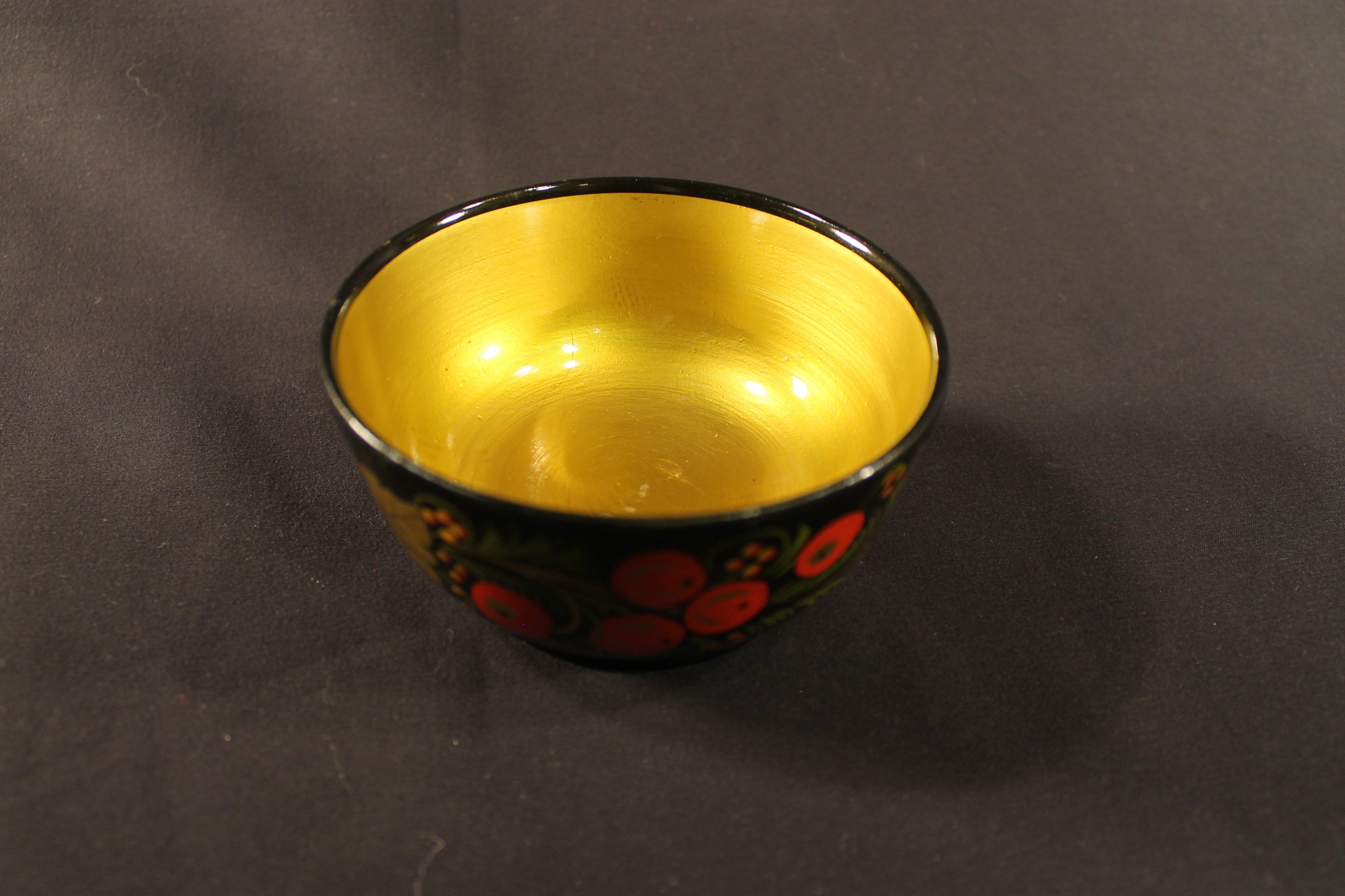 Small black lacquer bowl with interior gold. The exterior black has painted gold leaves, red apples, green grass design.