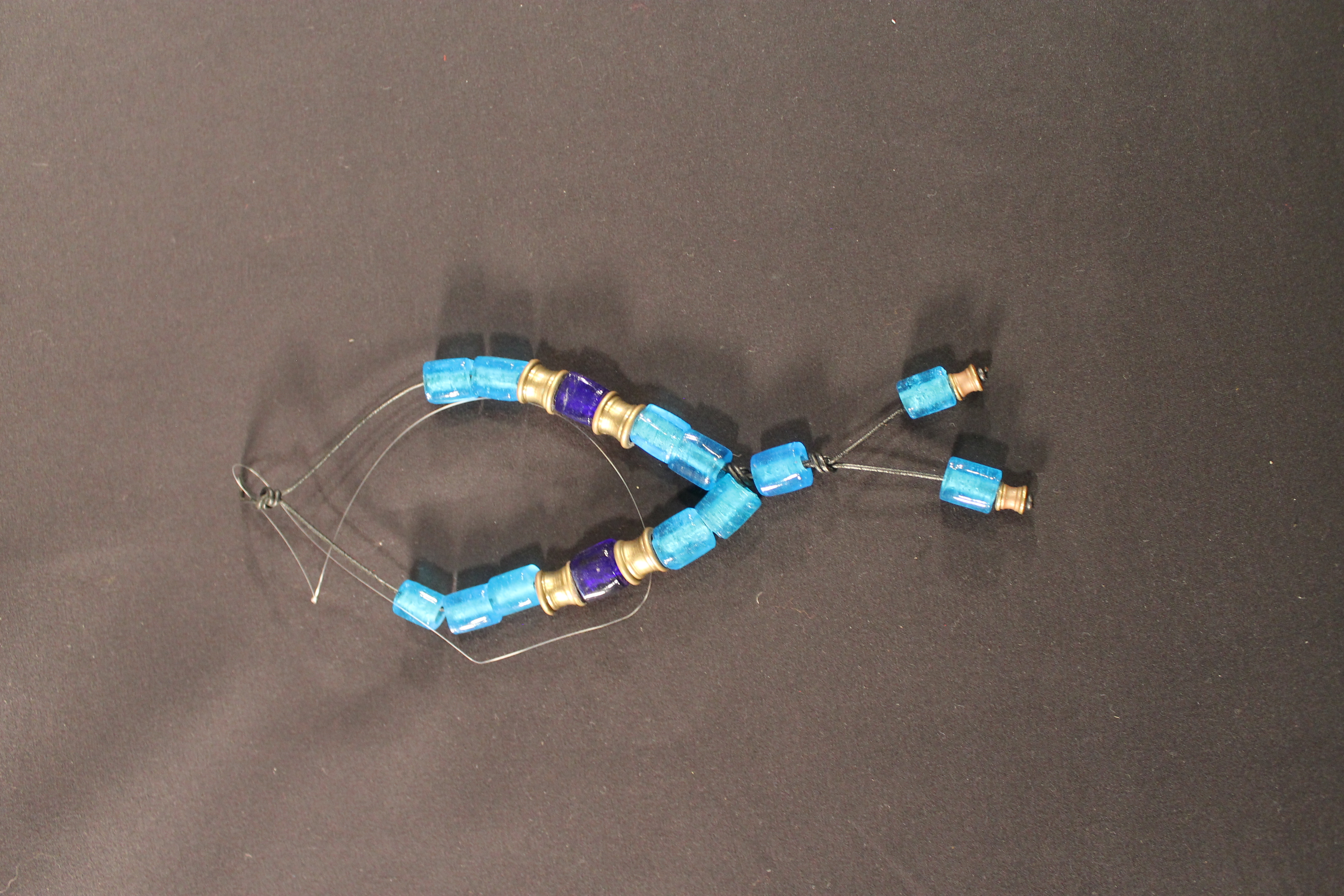 Transparent dark and light blue beads are attached to a black string with gold accent beads. 