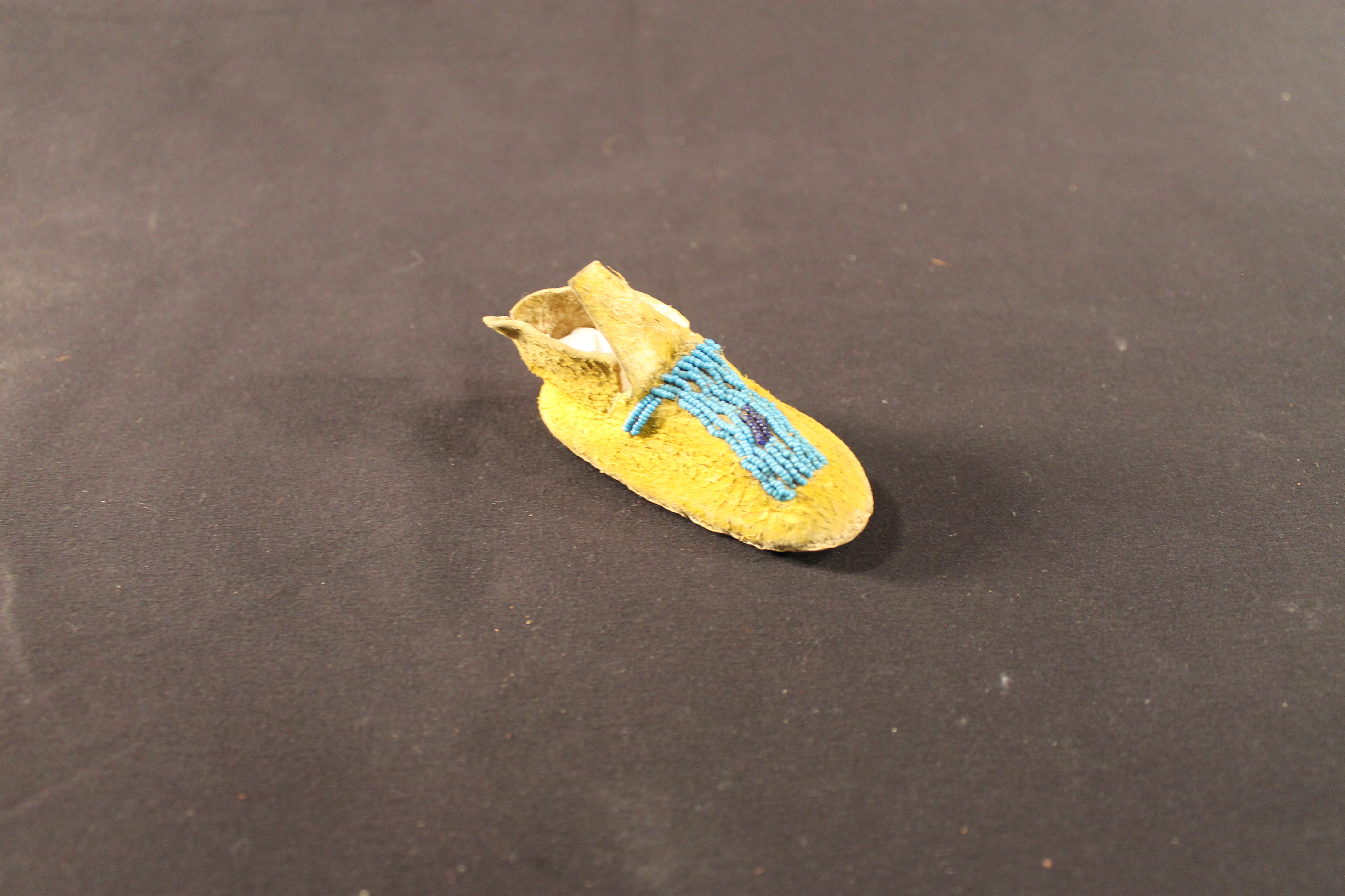Baby-sized moccasin with a decorated front turquoise with attached black beads.