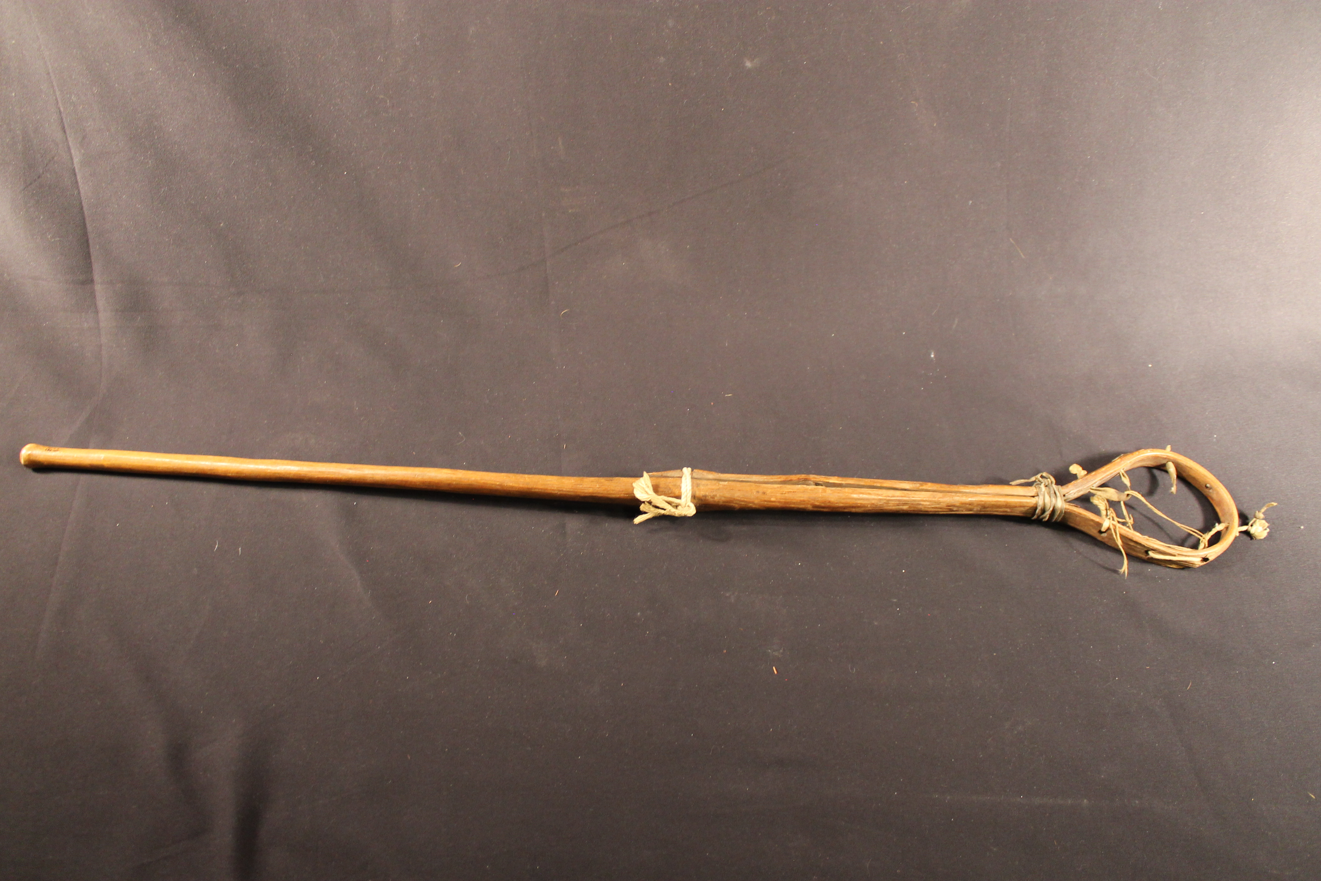 Lacrosse stick made of wood that has been bent into a loop at one end with a leather net in the center.