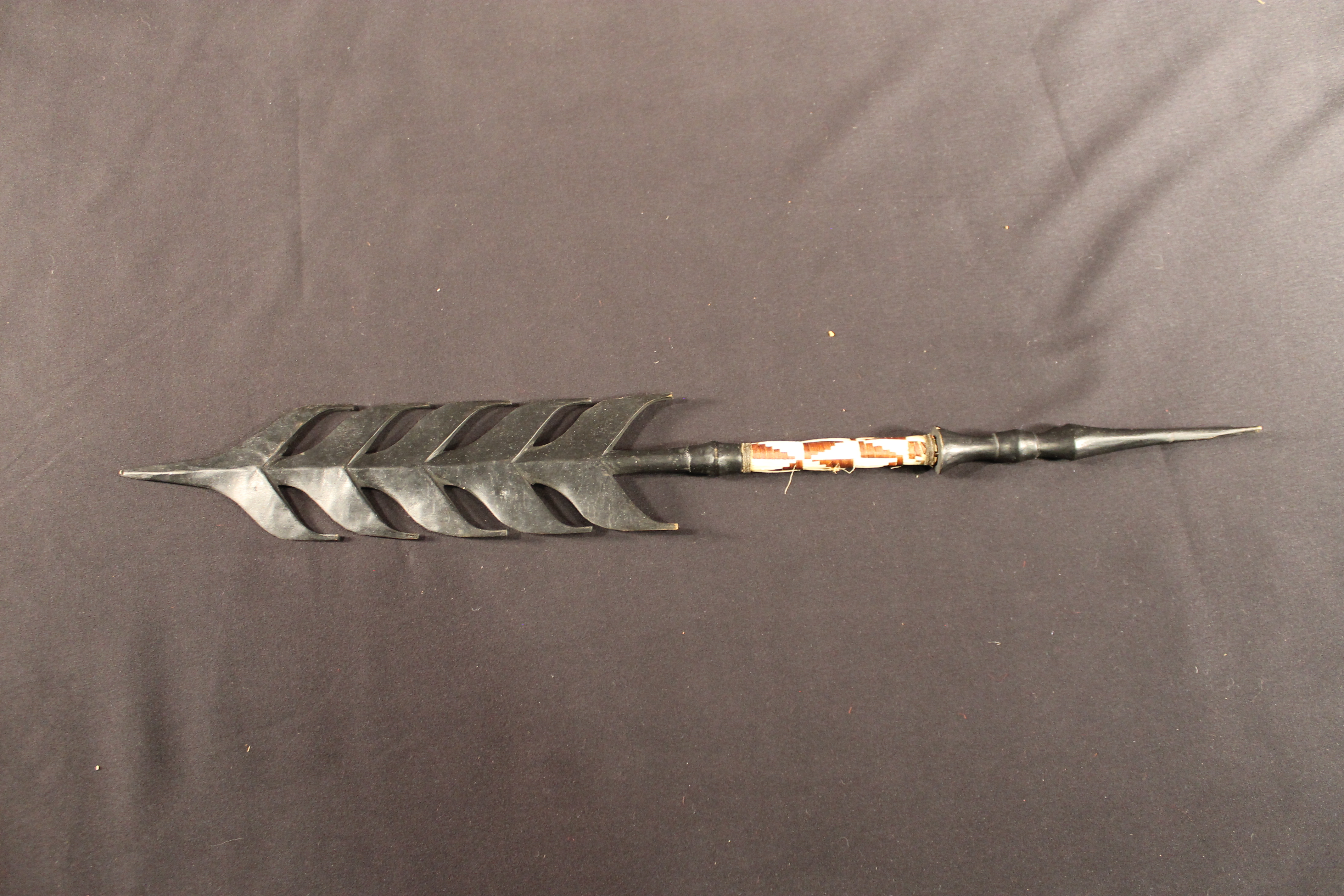Carved black wooden staff crest. A band in the center is covered with black and white woven straw.