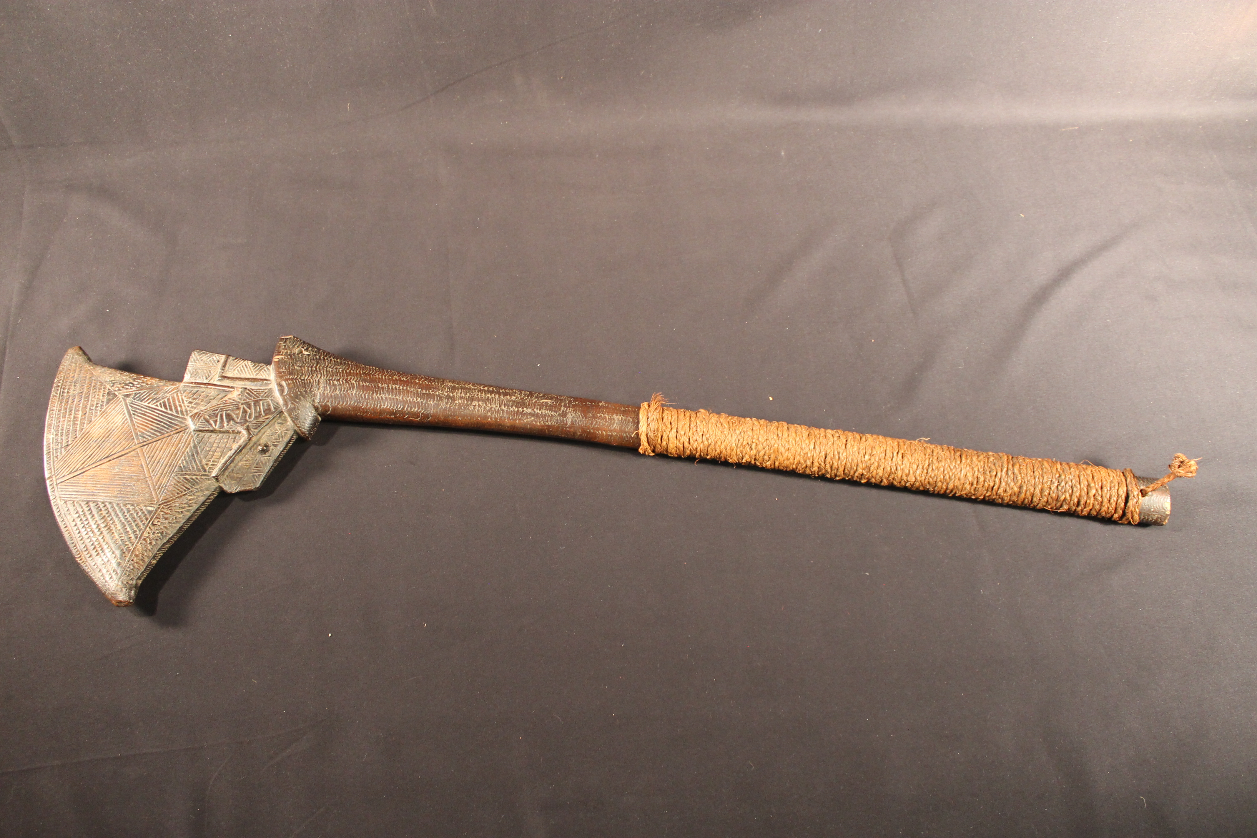 Wooden carved club decorated with diamond check pattern. The end of the club is wrapped in twisted fiber cord.