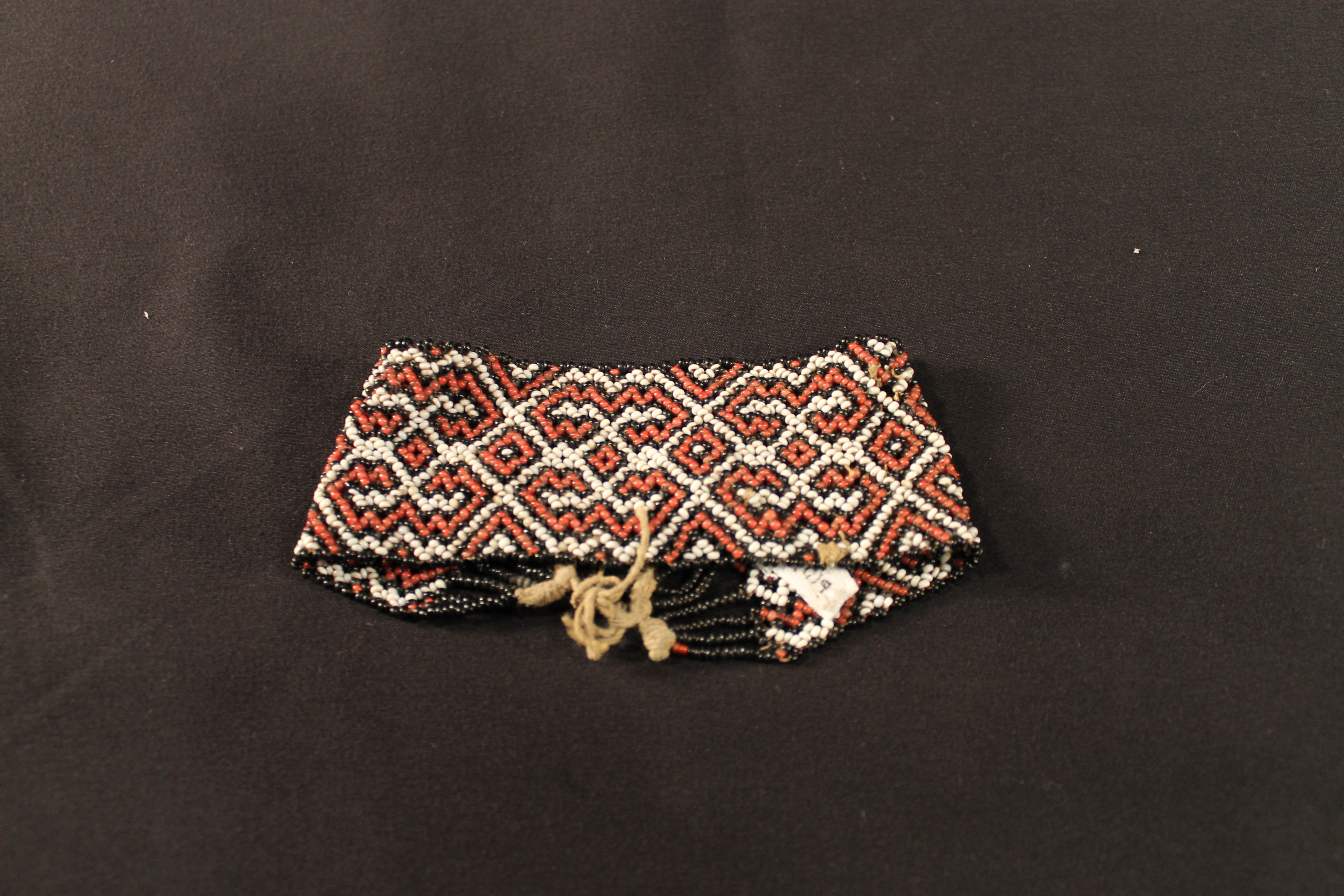 Loomed beadwork bracelet made of black, red, white beads. Tie closure on one side.
