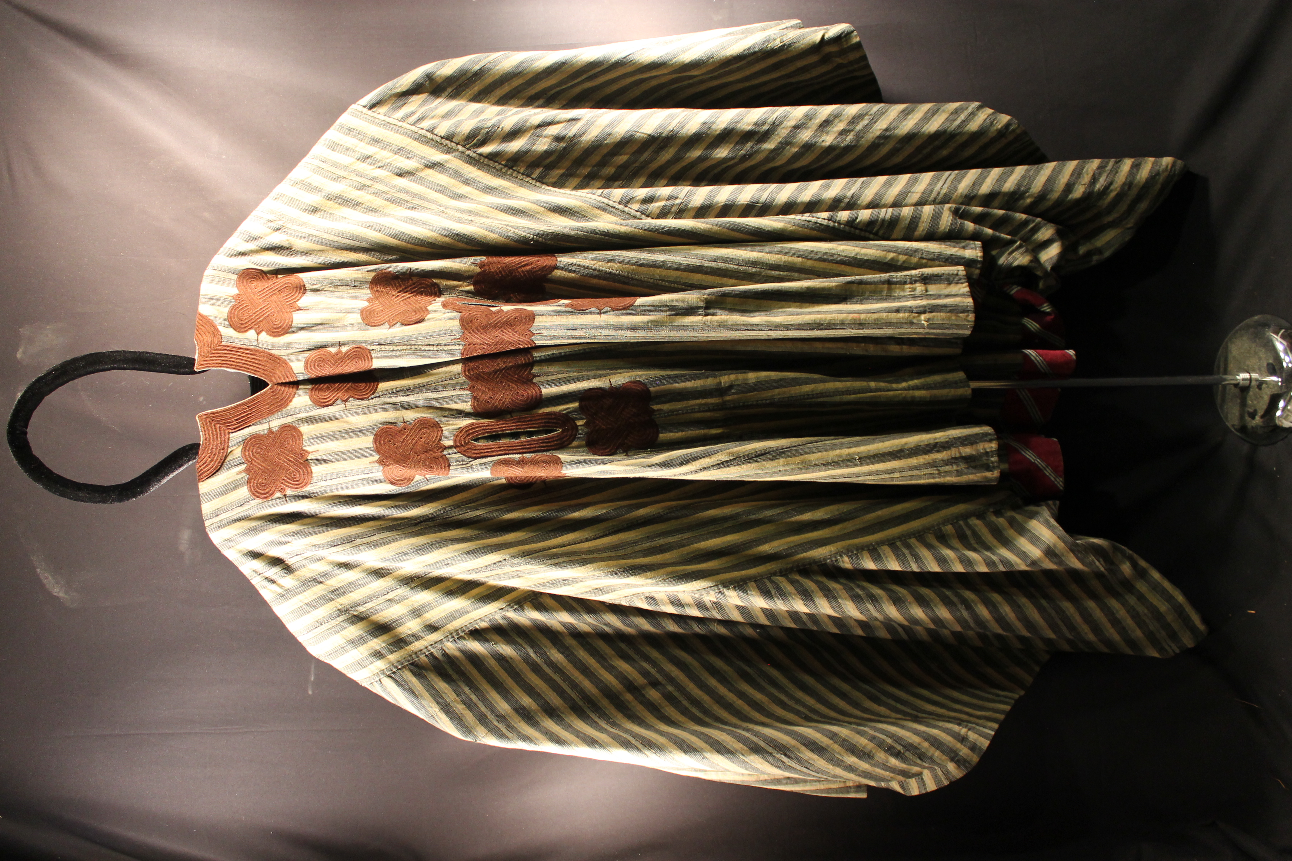 Robe made of green and tan stripe material. Brown embroidery around the neck and on the chest, depicting square patterns.