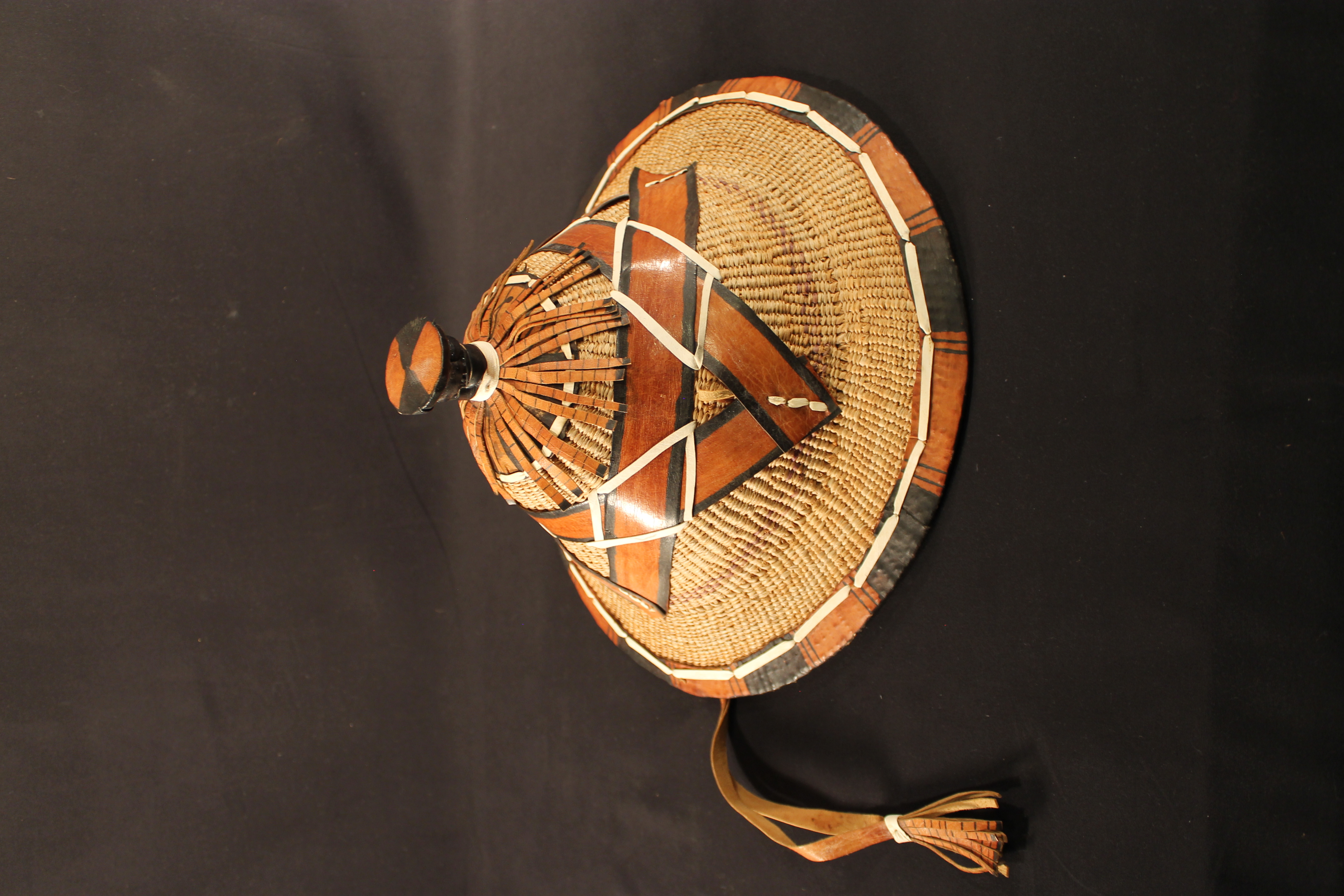 The hat is made of straw covered in leather design. The brim is covered by reddish/brown and black leather stitched in white leather, while the tip of the hat has a leather design to form a star. 