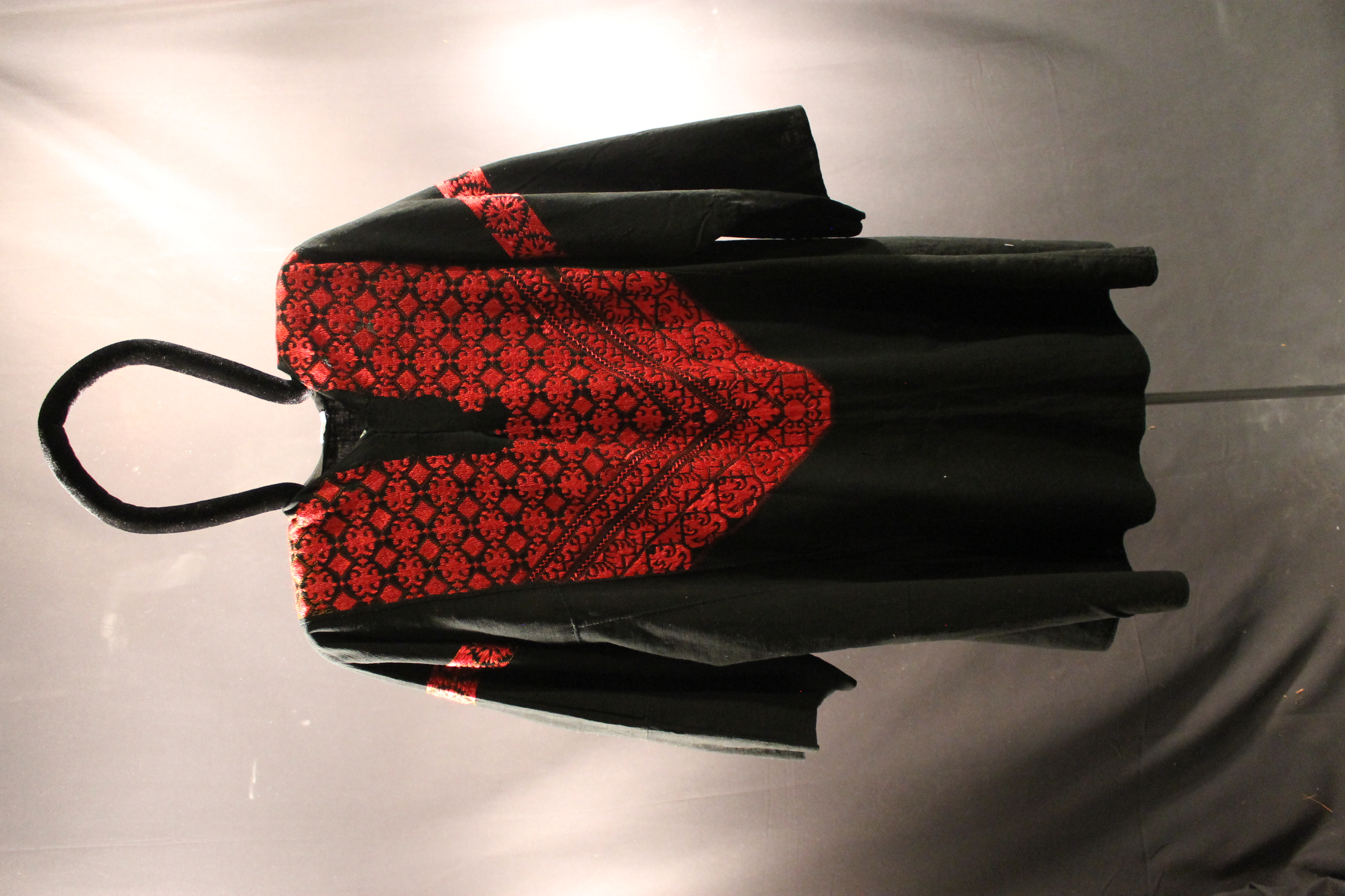 Black tunic with red embroidery of squares and flower-like shapes on the front. 