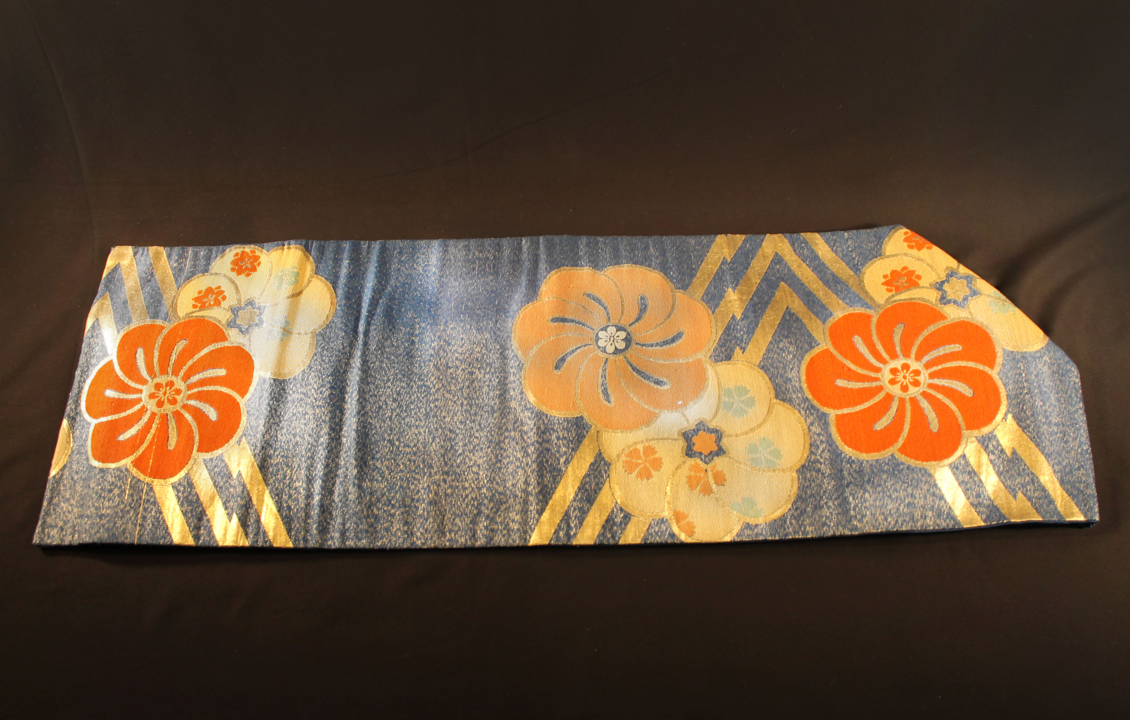  Blue fabric sash with gold and orange flower design. Gold threads are woven into the front blue fabric.