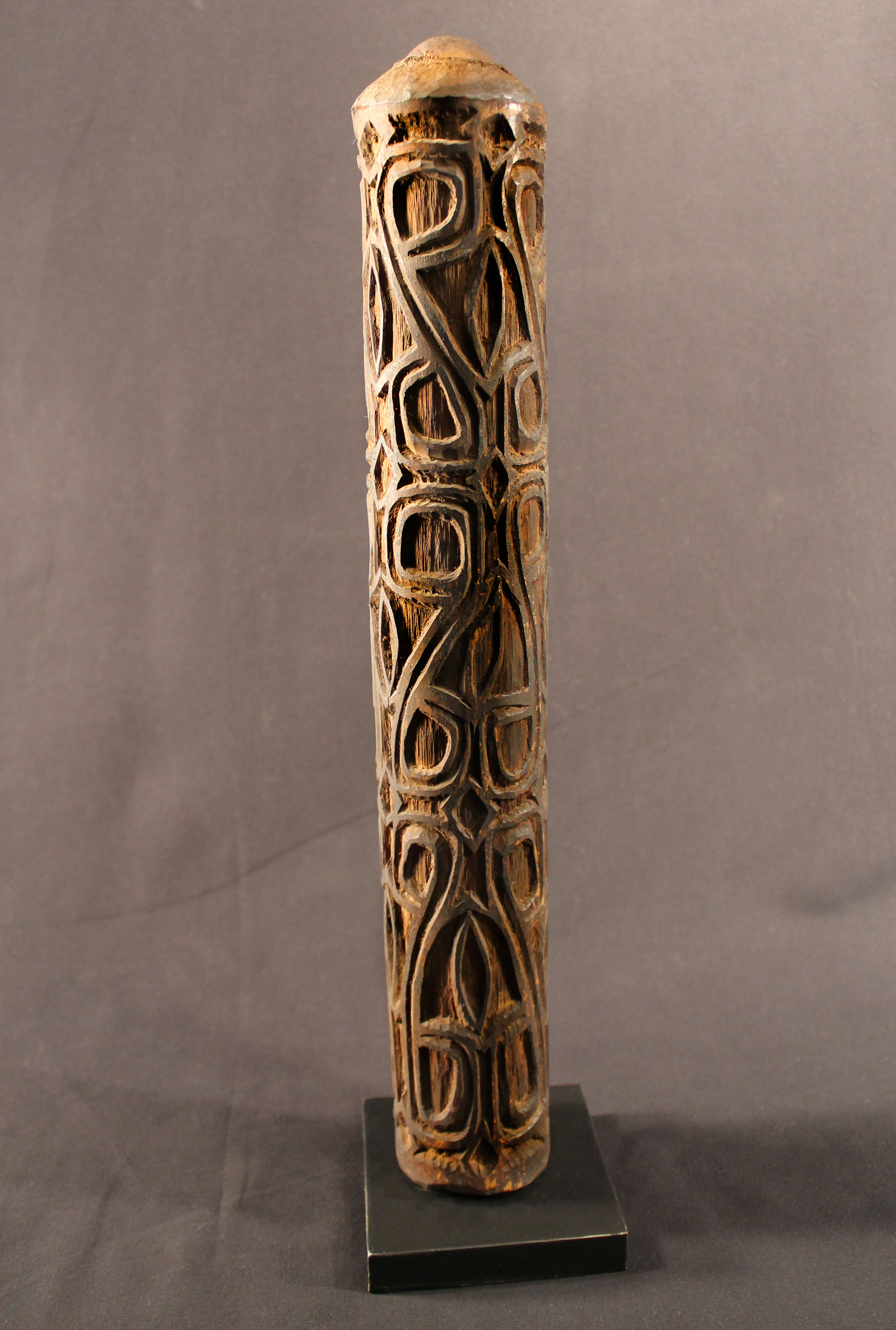 A long carved musical horn made of carved wood and is painted with charcoal, which helps the carved navel pattern to be seen. 