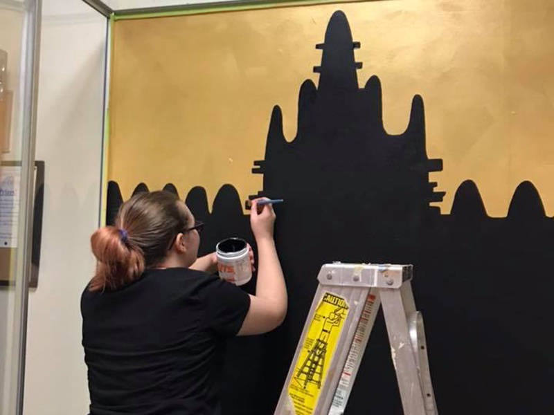 A student paints a backdrop for an exhibit