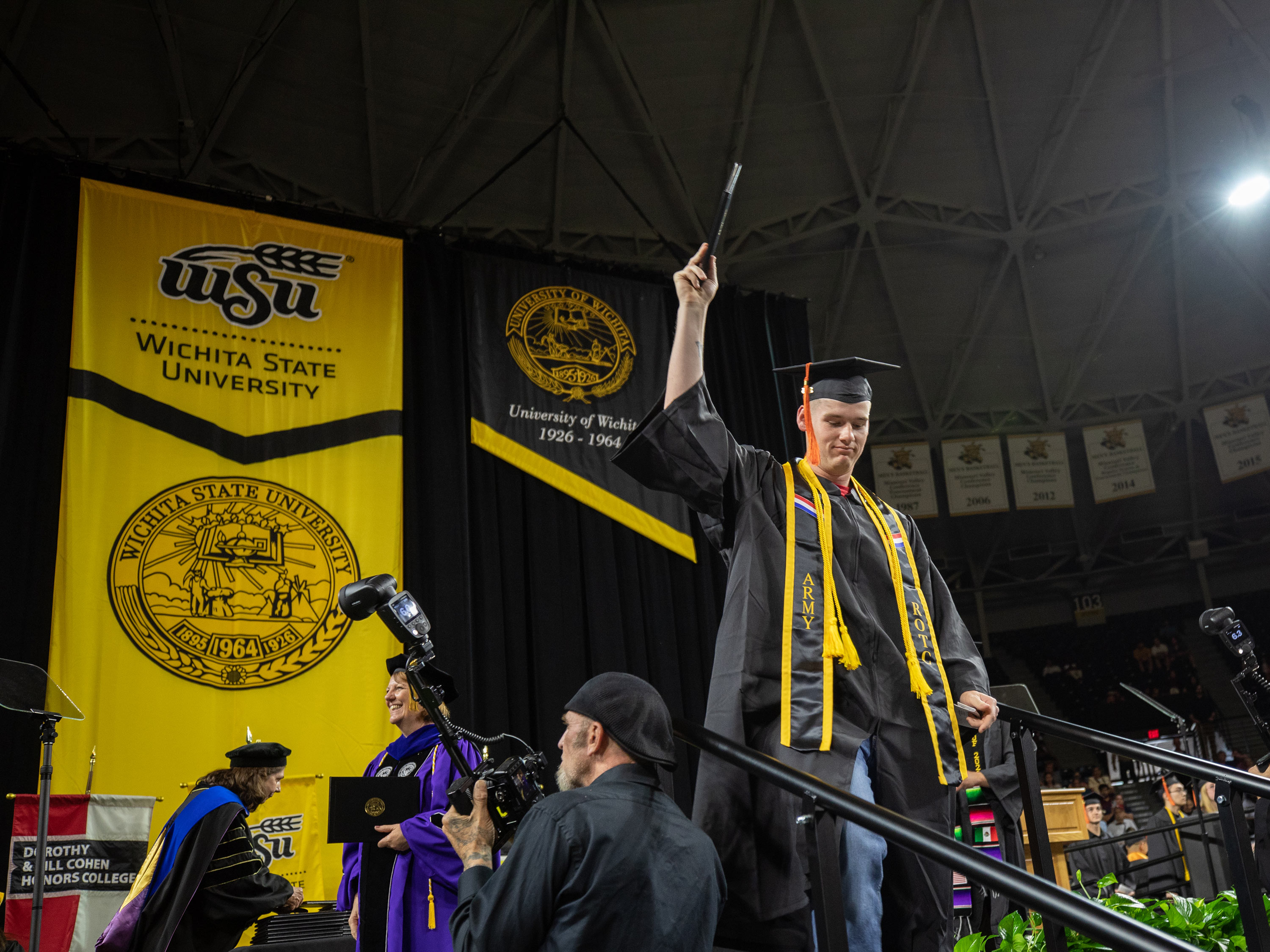 A student holds a diploma in the air while walking the stage at spring commencement.