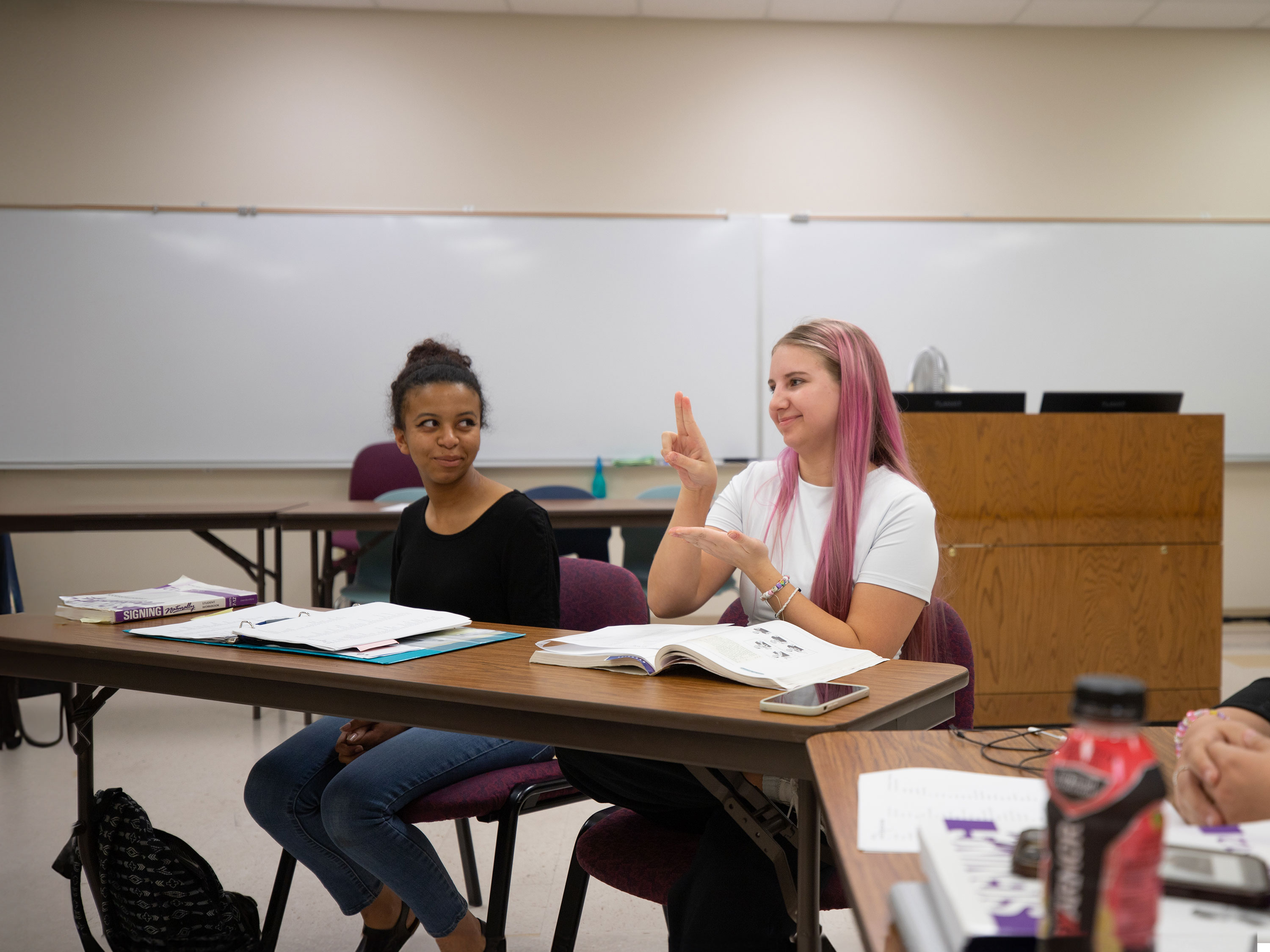 A student using American Sign Language while another student is looking at her in a classroom.