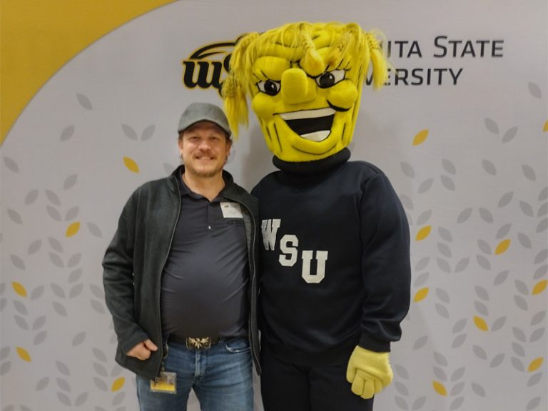 Photo of Daniel Ludlow standing at an event with the WuShock mascot. 