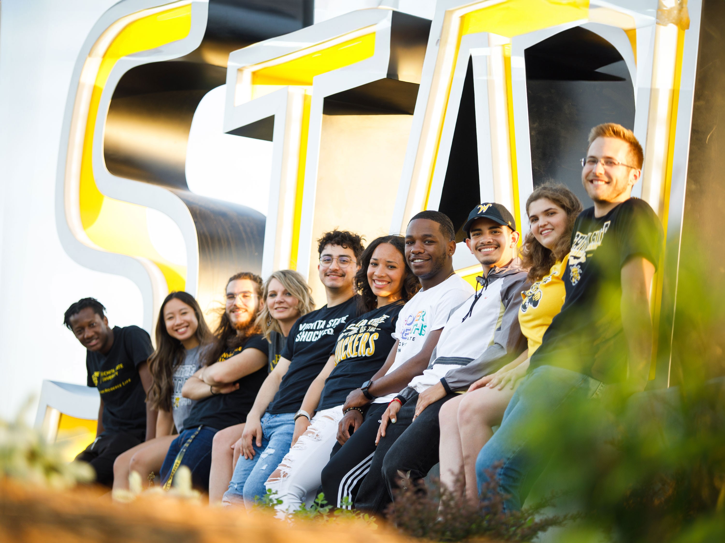 A group of students smiling together in front of the Wichita State sign.