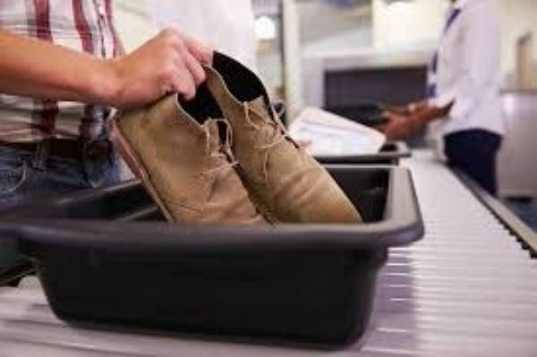 Person placing shoes in a bin at an airport security checkpoint conveyor belt for screening