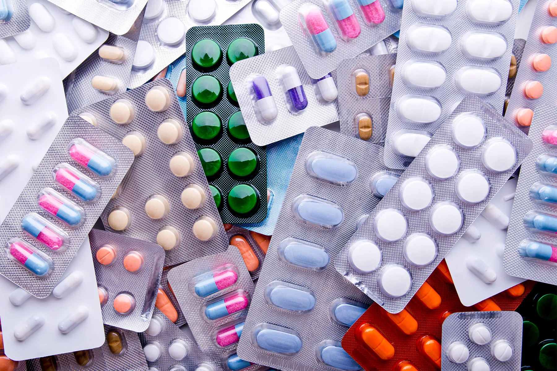 Various blister packs containing colorful capsules and tablets in different shapes and sizes, scattered in a pile.