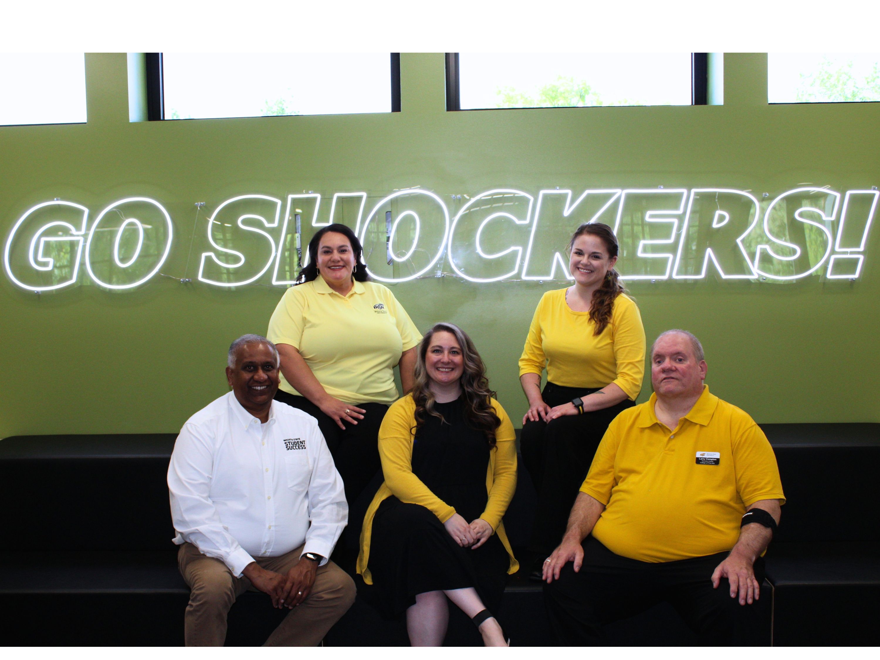 coaches sitting in front of go shockers sign in the shocker success center