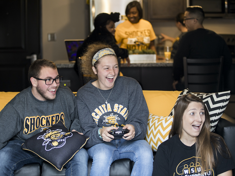 Three students happily playing video games while sitting on a couch. 
