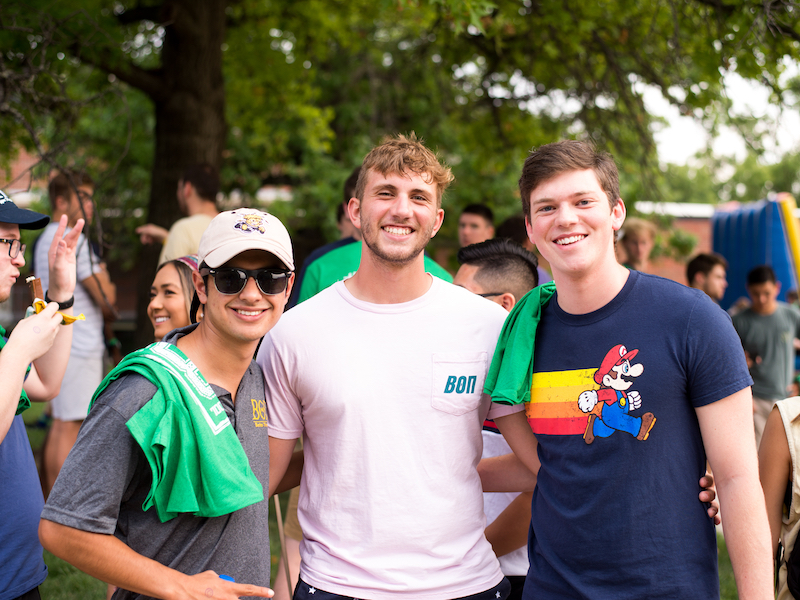 Photo of three male students smiling for the camera at an outdoor event. 