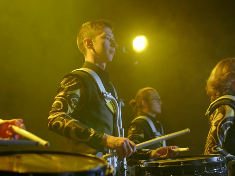 A shocker sound drum line member is pictured in a studio with yellow lighting