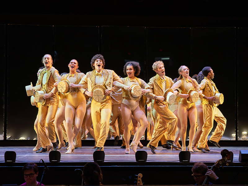 An ensemble of student actors on stage dressed in gold costumes