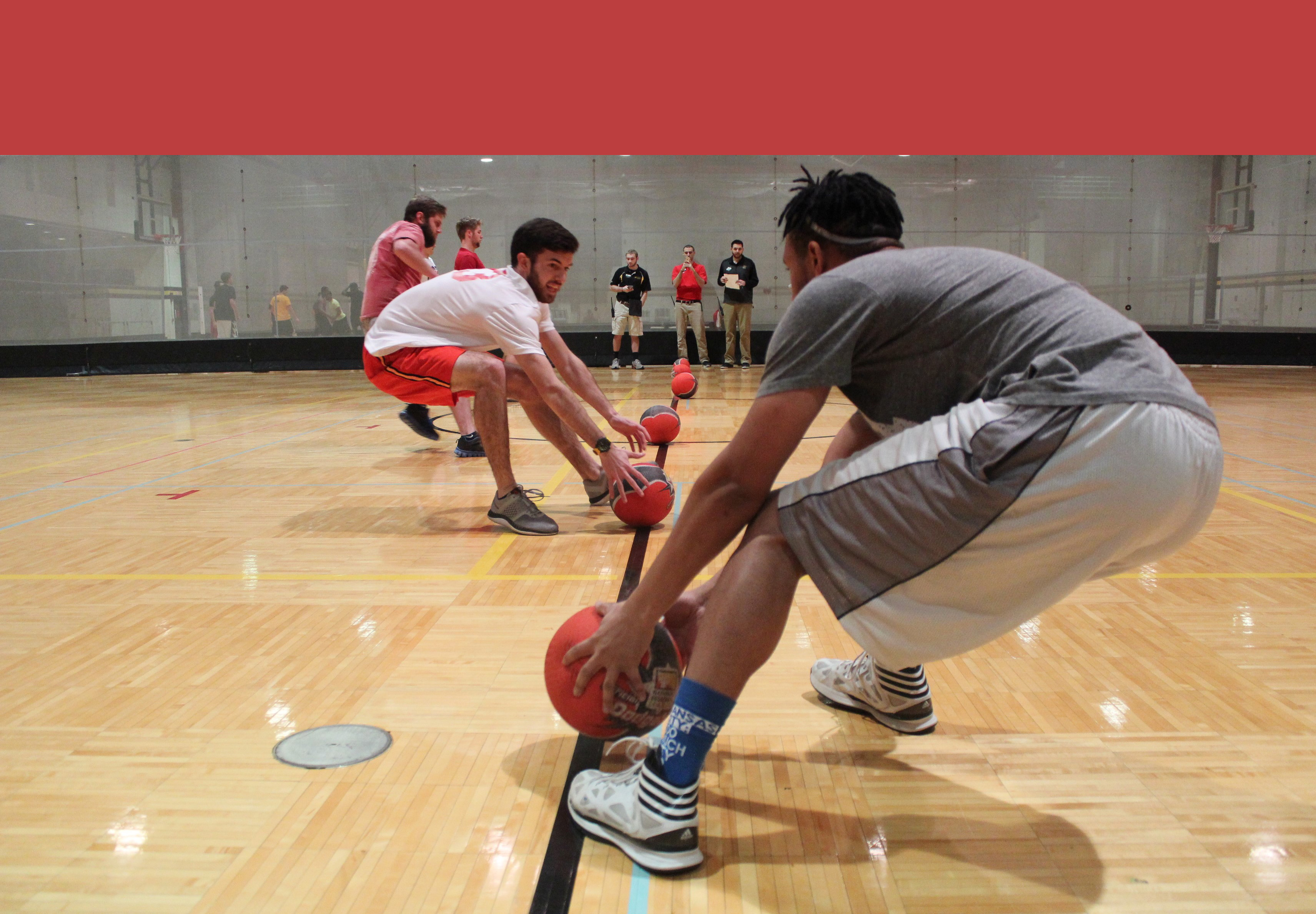 Beginning of a dodgeball match; two boys grab balls on the centerline, poised to spring away back onto their side, away from the opponent.