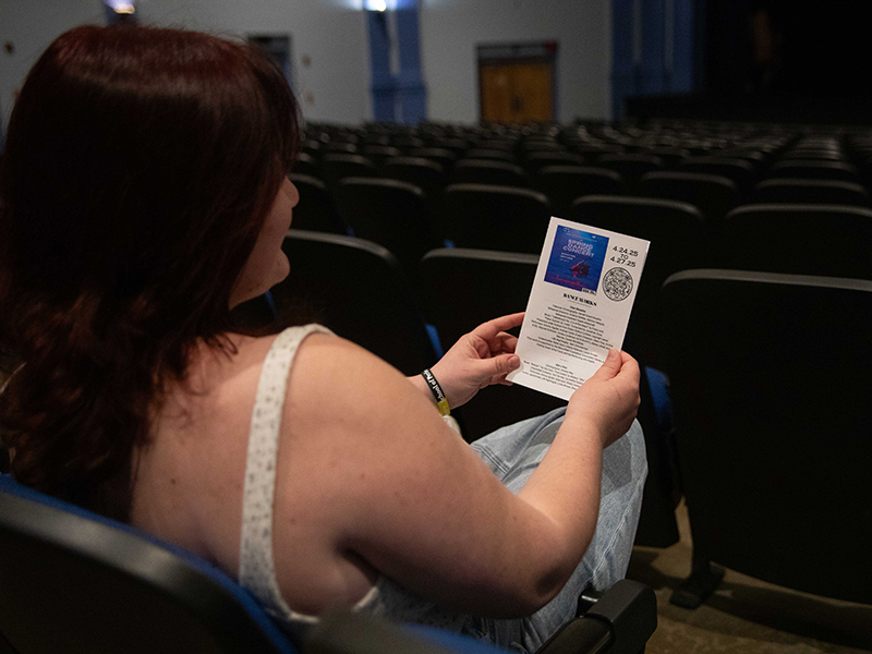 Alexandra Enmark sit in the Wilner Auditorium where she works as a student intern holding up a program she helped create.