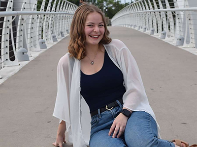 Photo of a student sitting on a bridge smiling at the camera