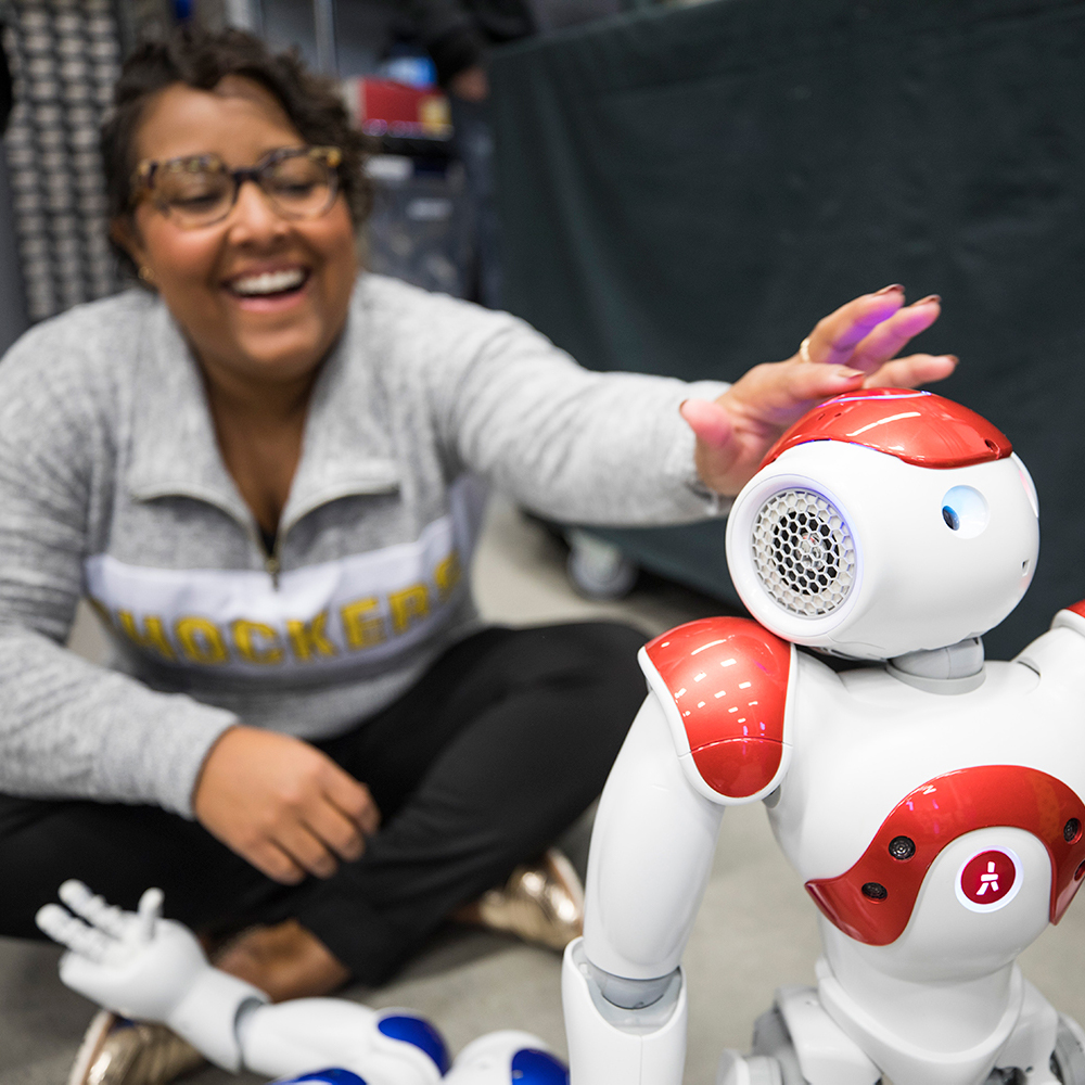 Photo of a woman smiling and reaching out to touch a robot
