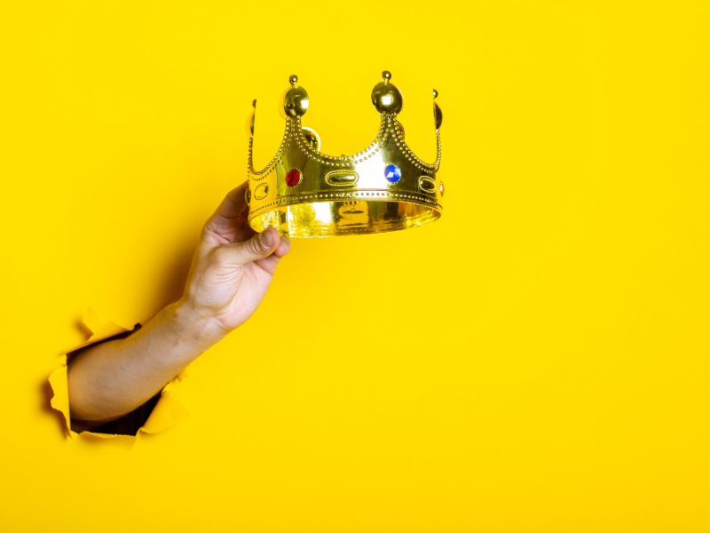 Hand holding a crown against a yellow background